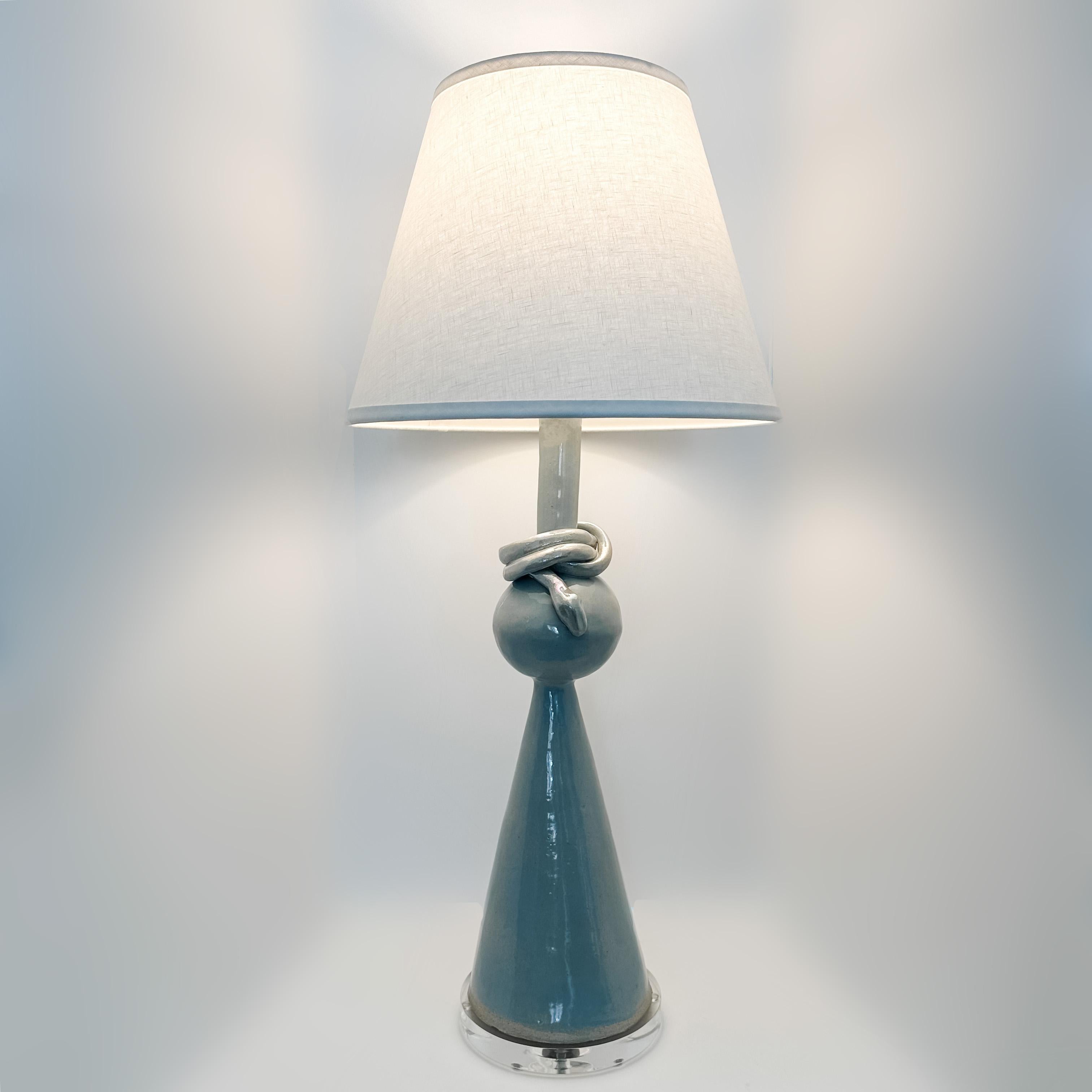 The Geo table lamp is handmade in raku clay in a Wedgwood glaze with silver components, braided silver fabric cord, and an ivory linen shade. Simple forms and clean design define the Geo Table Lamp. This understated design will complement any