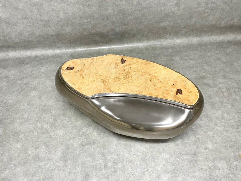 The Geode coffee table is carved in oak which is sheathed with (patinated and waxed) titanium. The tray is made of waxed natural maple burl veneer. It can either be attached to the table top or fixed on a rod so that it can rotate about an axis. The