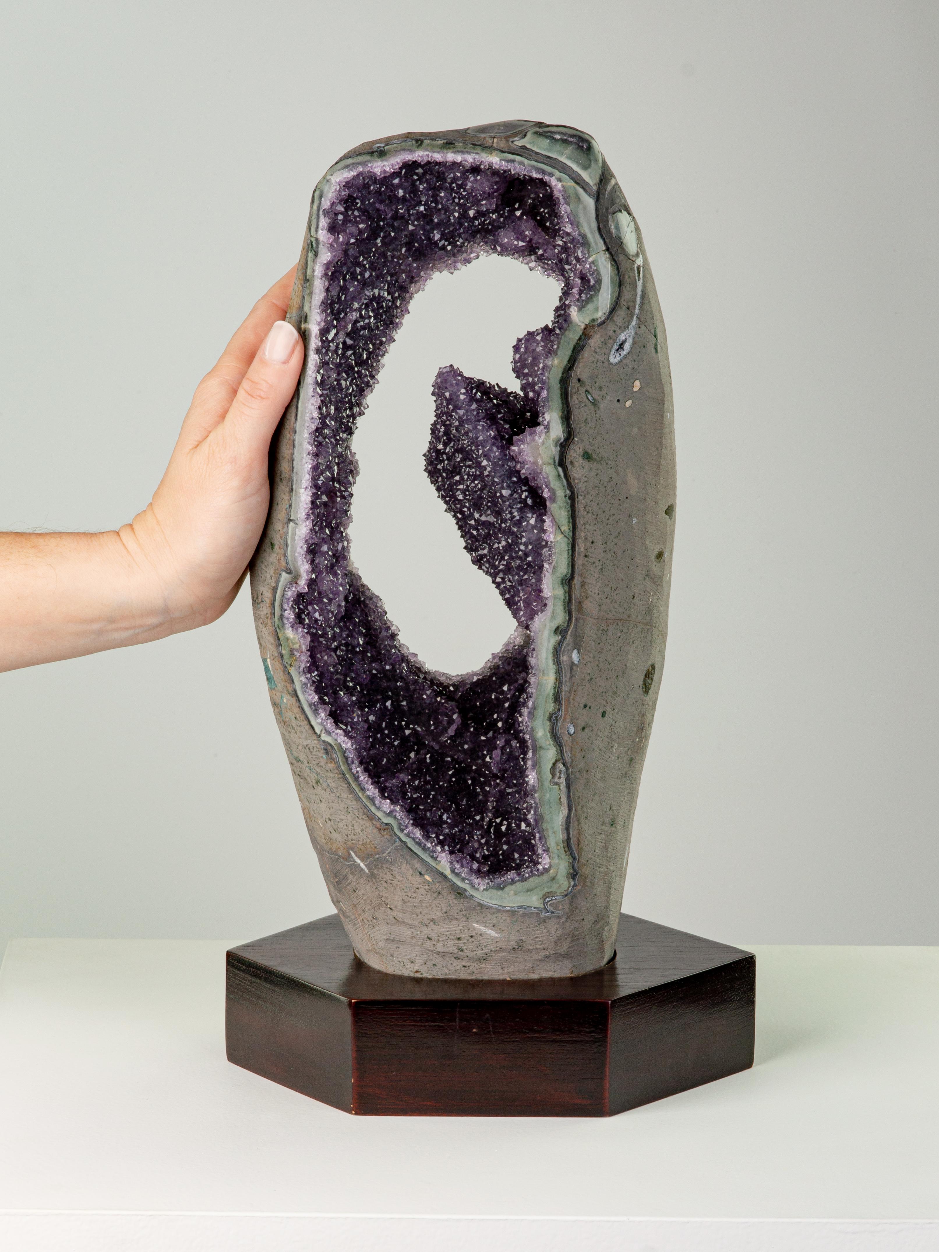 This striking section cut from the centre of a geode, contains an unusual formation of calcite with a blanket of amethyst crystals. The borders are polished to reveal the beautiful celadonite shell.

This piece was legally and ethically sourced