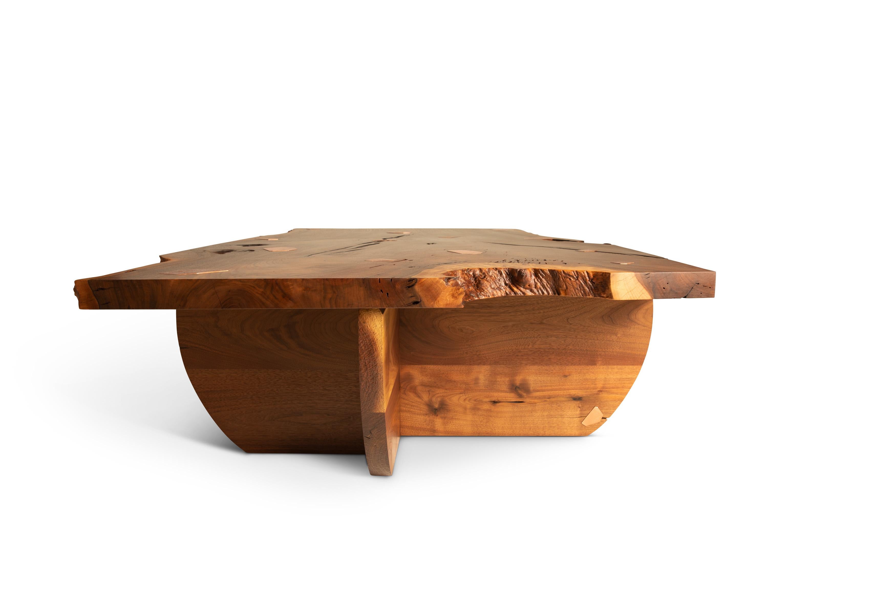 Sculptural coffee table featuring a claro walnut top with copper inlays and a hand shaped black walnut base