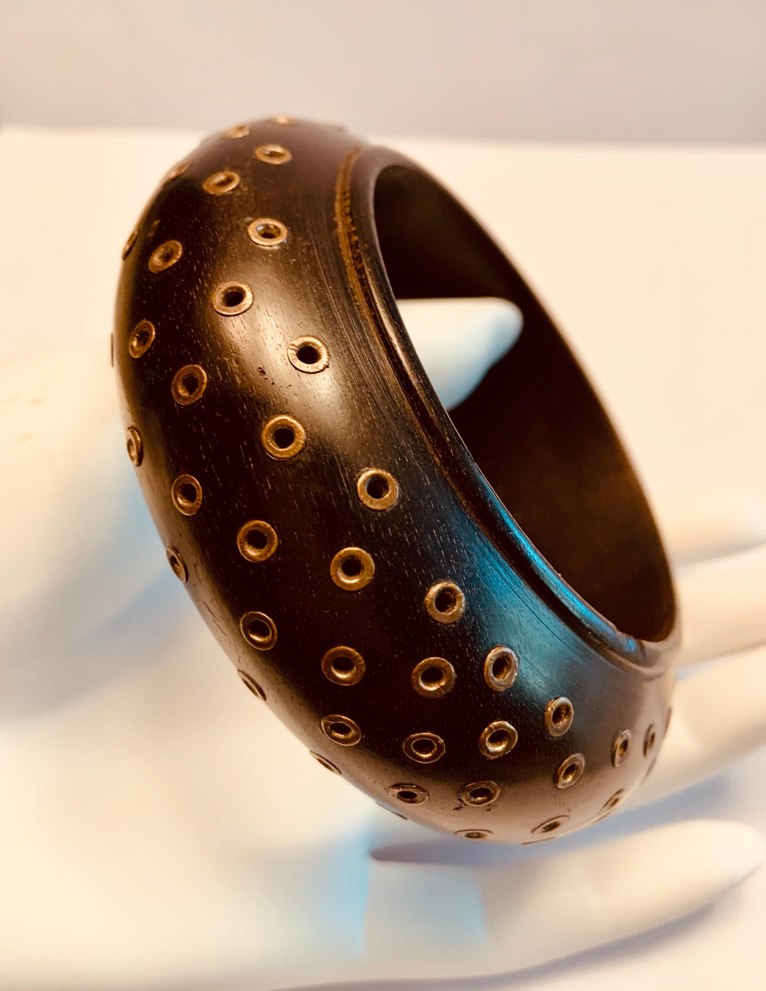 This great wood bracelet from the Geoffrey Beene Archives is studded with brass edged openings. It is a smooth dark hardwood, with one small rough patch at the edge. The Archive inventory number is still on the inside of the bracelet. 
It was most