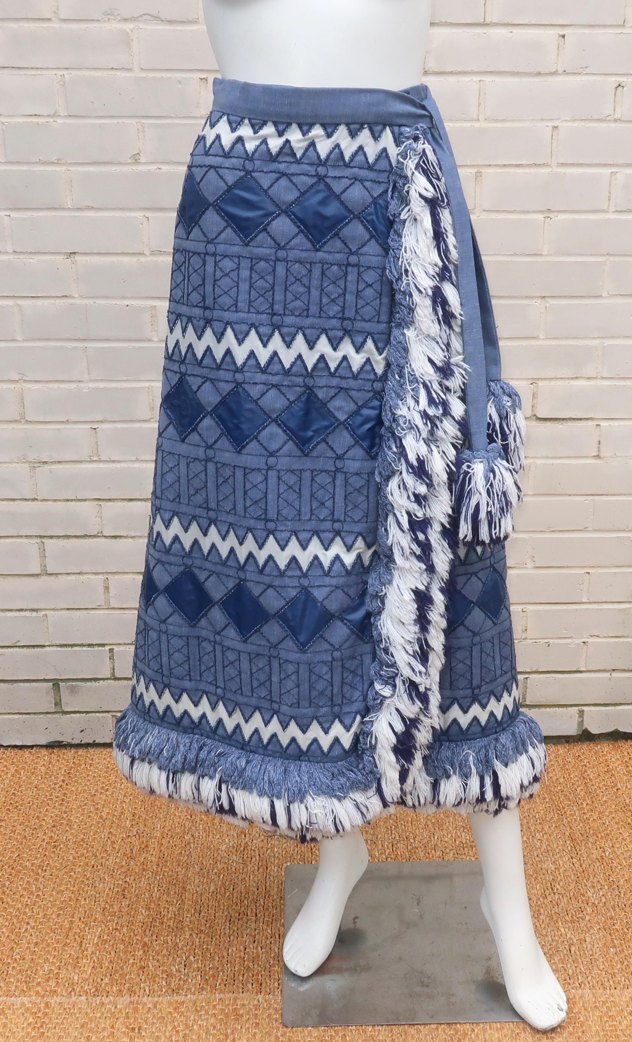 Late 1960's Geoffrey Beene denim wrap skirt with a geometric design accented by shiny blue and white nylon fabric as well as rows of yarn embroidery and heavy fringe.  The front wrap silhouette is held closed by a hidden band of velcro (an exciting