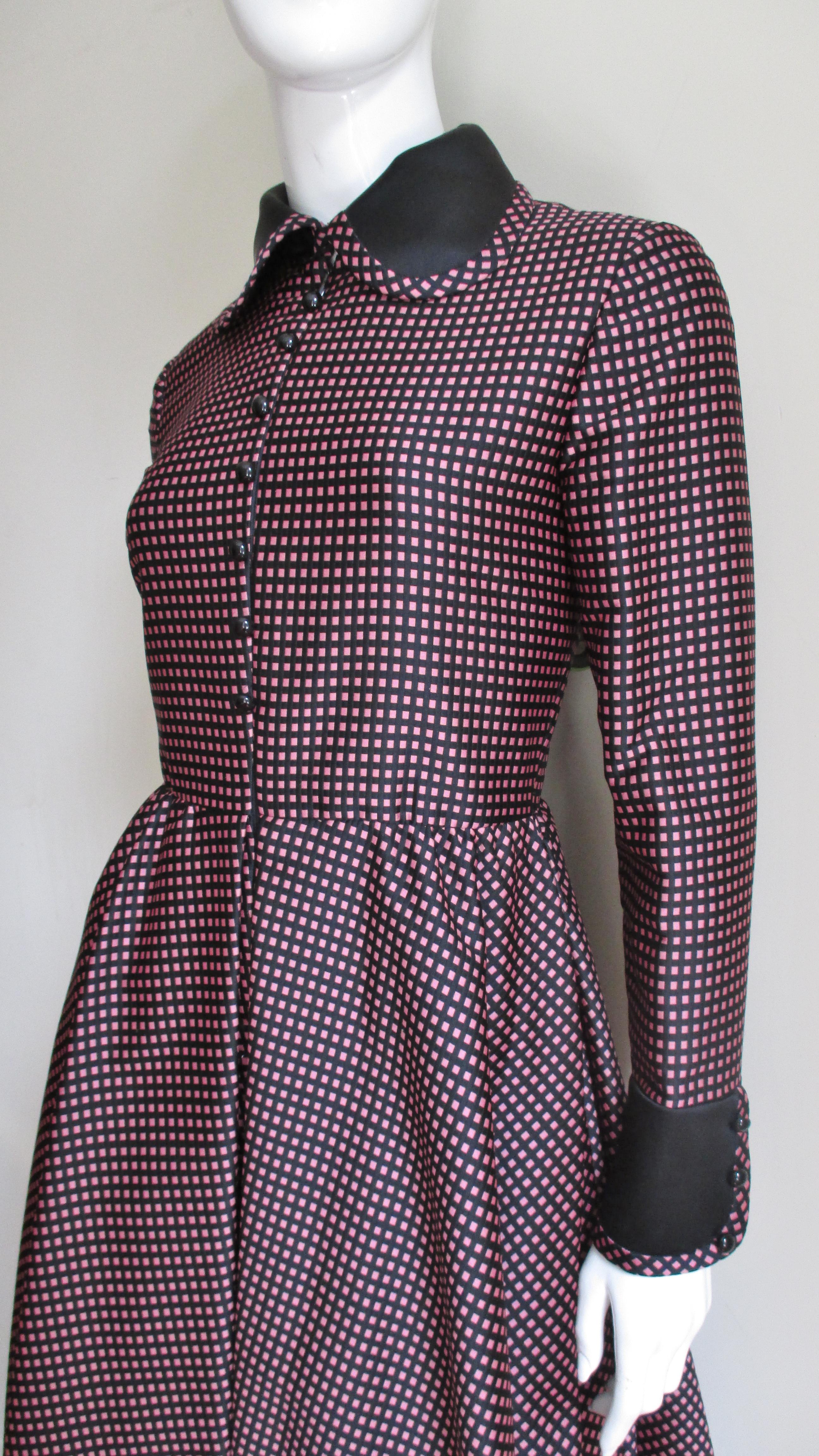 A charming silk dress in a pink/black check from Geoffrey Beene. It has a black Peter pan collar, side seam pockets, black button cuffs on long sleeves and round black decorative buttons up the front over a zipper closure. The bodice is fitted with
