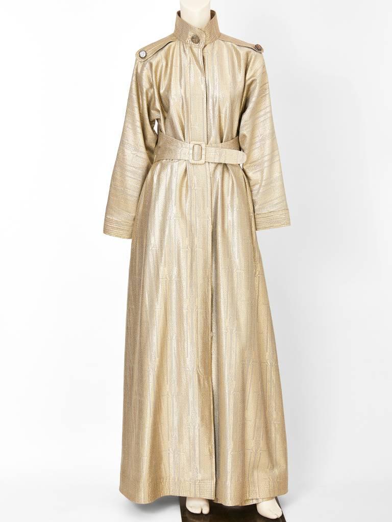 Geoffrey Beene, gold lame evening, belted trench - style dress with matching pant ensemble. Trench has epaulettes at the shoulders that attach at the shoulders with a button and a mandarin style collar. Epaulettes, collar, belt and sleeve cuffs have