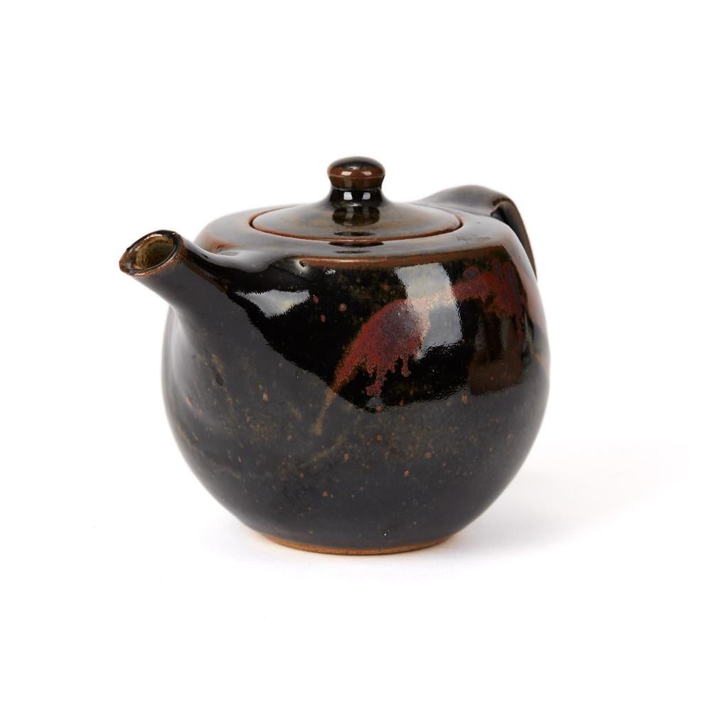 A vintage studio pottery teapot made at Avoncroft Pottery by Geoffrey Whiting. The teapot of squat rounded form is decorated in tenmoku glazes in dark brown and copper colors. The teapot has a recessed cover and has an impressed seal mark below the