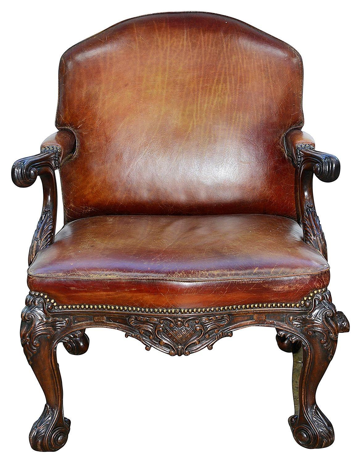 Très beau fauteuil en cuir d'acajou de style 18e siècle, dont le cuir est d'une magnifique couleur fauve décolorée, avec des clous en laiton. Décor classique de volutes et de feuillages sculpté à la main sur le bois apparent, reposant sur quatre