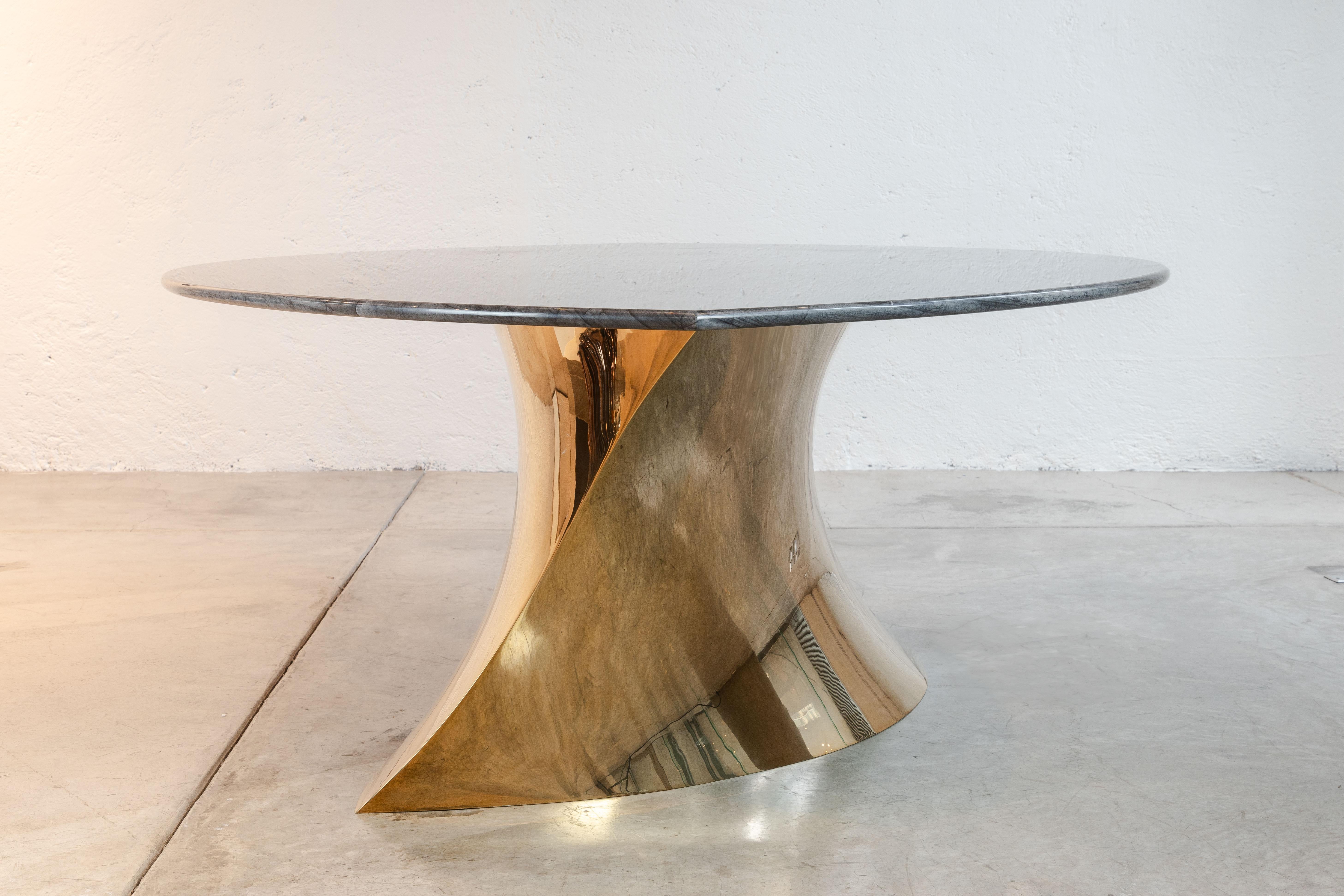 Der Geometra Esstisch von Katz Studio ist ein minimalistisches Statement, das die reflektierende Eleganz eines polierten Bronzefußes mit der robusten Schönheit von Adamantium-Granit verbindet. Die geometrische Form und die spiegelnde Oberfläche