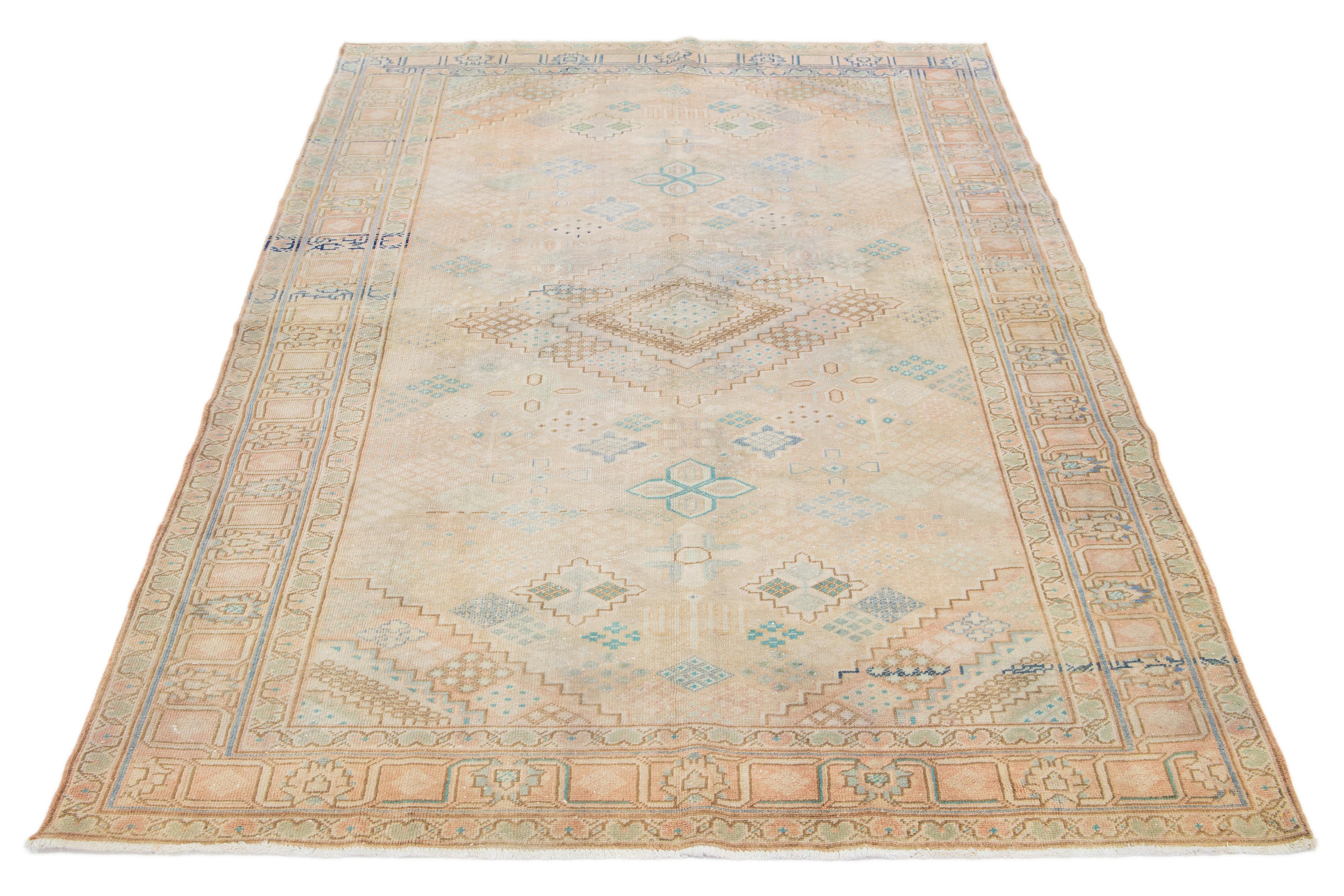 This Josheghan Persian wool rug boasts a captivating antique allure. Meticulously hand-knotted using premium quality wool, it features an alluring beige field with peach, green, and blue accents arranged in a mesmerizing all-over geometric
