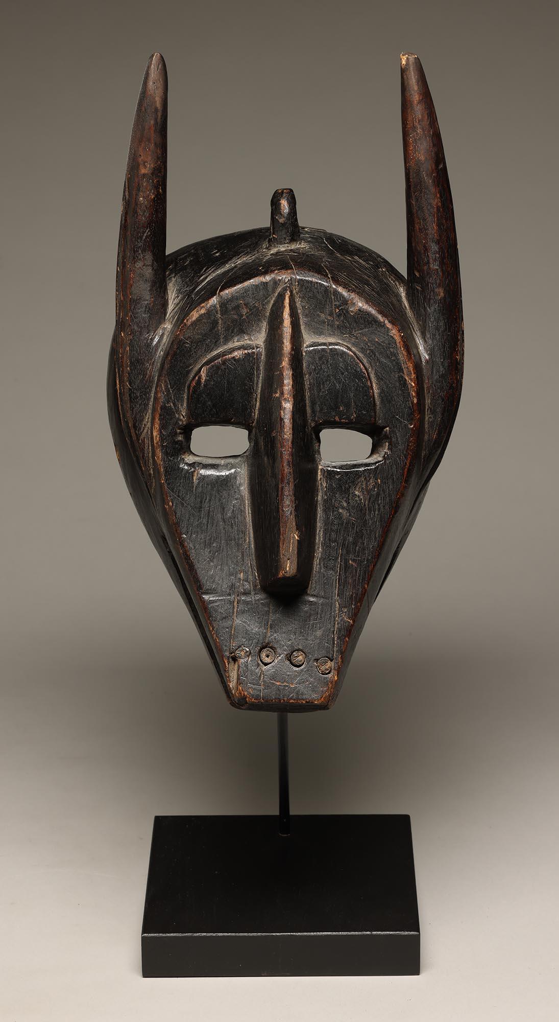 Geometrische Barmbara Sukuru Tiermaske mit Hörnern, Zähnen, Mali, Westafrika.  Eingesetzte Holzzähne, abstraktes Gesicht mit offenen Augen, hochgezogenen Augenbrauen und gerahmtem Gesicht.  Alte einheimische Reparatur mit Eisenstreifen auf der