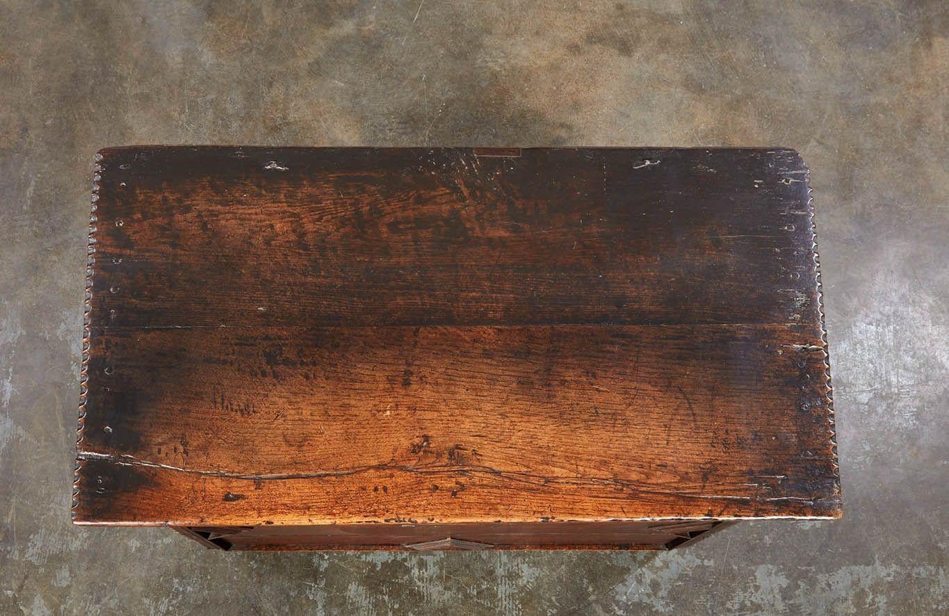 Una cassapanca per coperte o cassette di sicurezza, con piano incernierato sul davanti con decorazioni geometriche modellate, lati leggermente inclinati con piedini sagomati integrali e schienale a listelli. Presenta cerniere originali in ferro