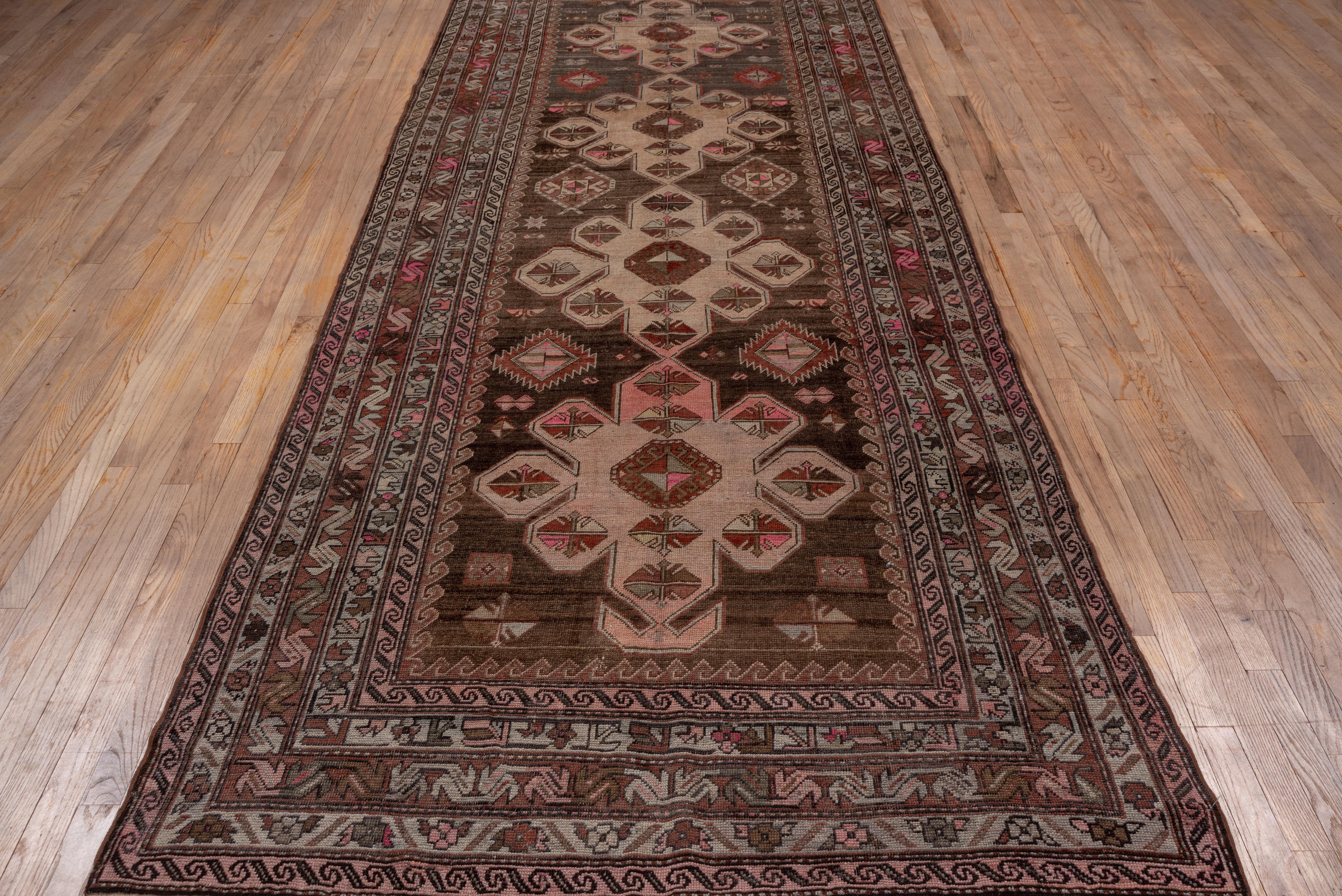 From the border area between Persia and the Caucasus, this geometric gallery carpet features four eight-lobed, connected medallions in sand and straw on an abrashed red-brown ground, with central hooked octagon motives. Hexagons and ashiks decorate