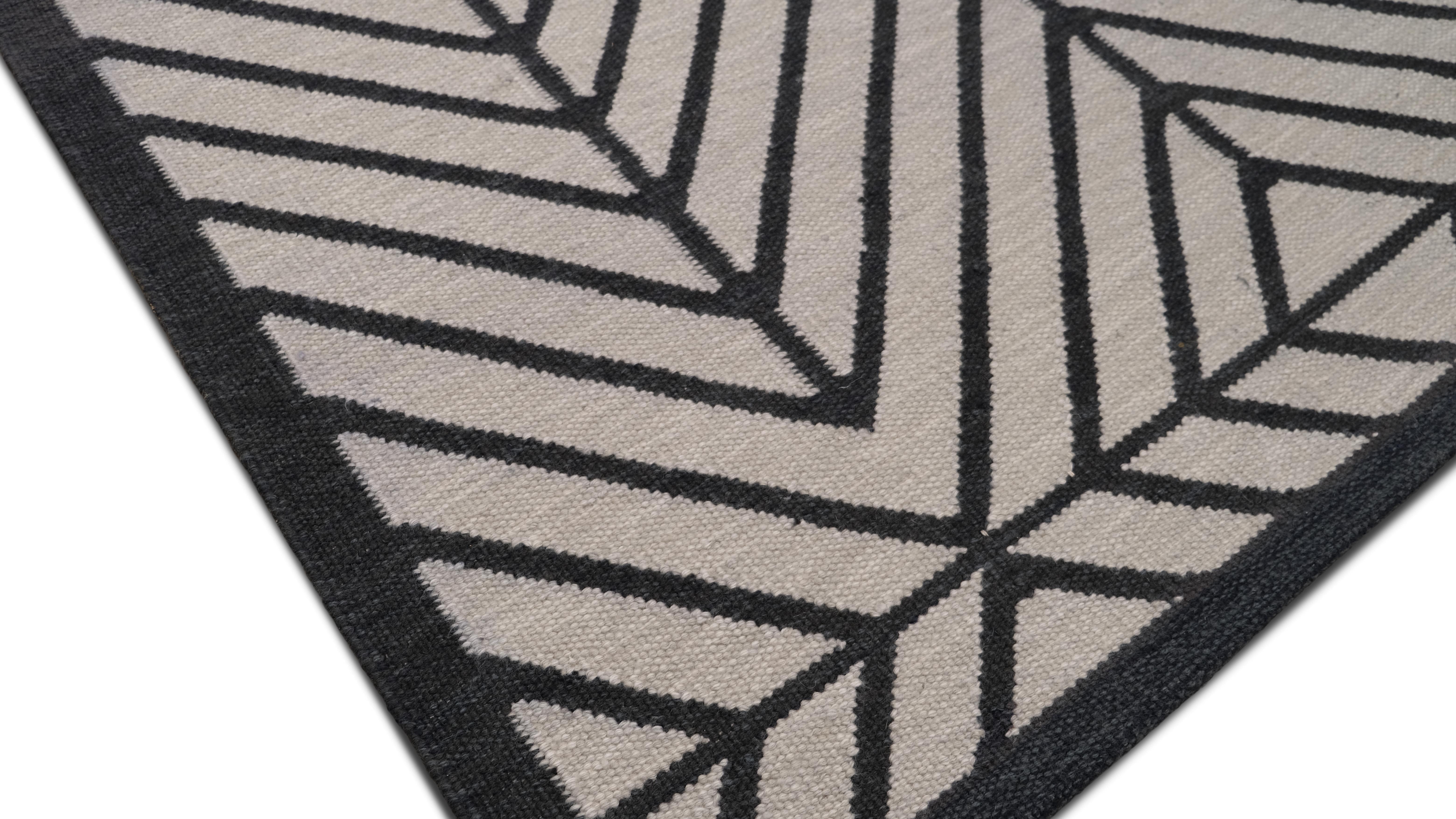 Dieser handgeknüpfte Wollteppich zeigt ein auffälliges geometrisches Muster in Charcoal Grey mit scharfen Chevron- und linearen Motiven, die einen fesselnden visuellen Kontrast bilden. Das kühne symmetrische Design, das durch eine strukturierte
