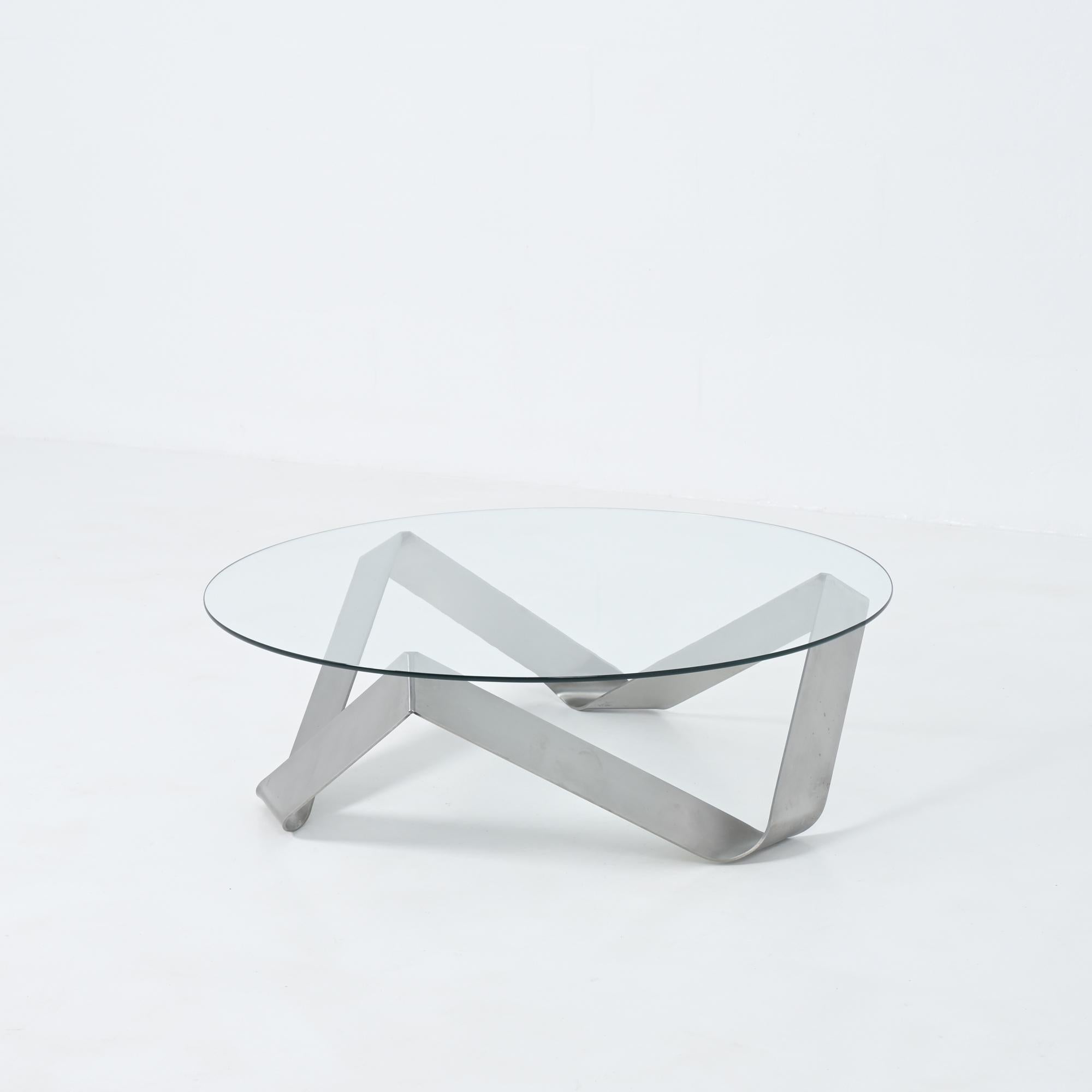 Cette table basse possède un plateau en verre soutenu par un cadre géométrique cohérent.

Le cadre est formé à partir de feuilles d'acier inoxydable pliées.

La table est en bon état.