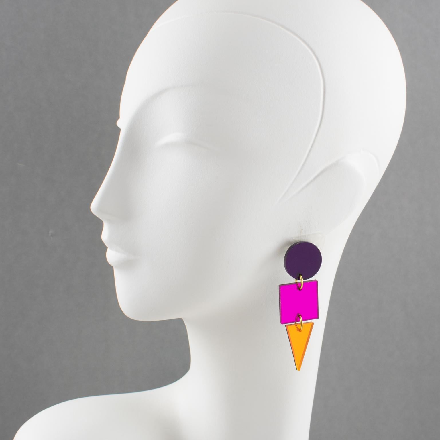 Diese wunderschönen Ohrringe aus Lucite haben eine flache, geometrische Form mit Farbblockfarben und spiegelnden Mustern in Neonorange, Pink und Lila. Diese Stücke sind für gepiercte Ohren. Es gibt keine sichtbare Herstellermarke. 
Abmessungen: