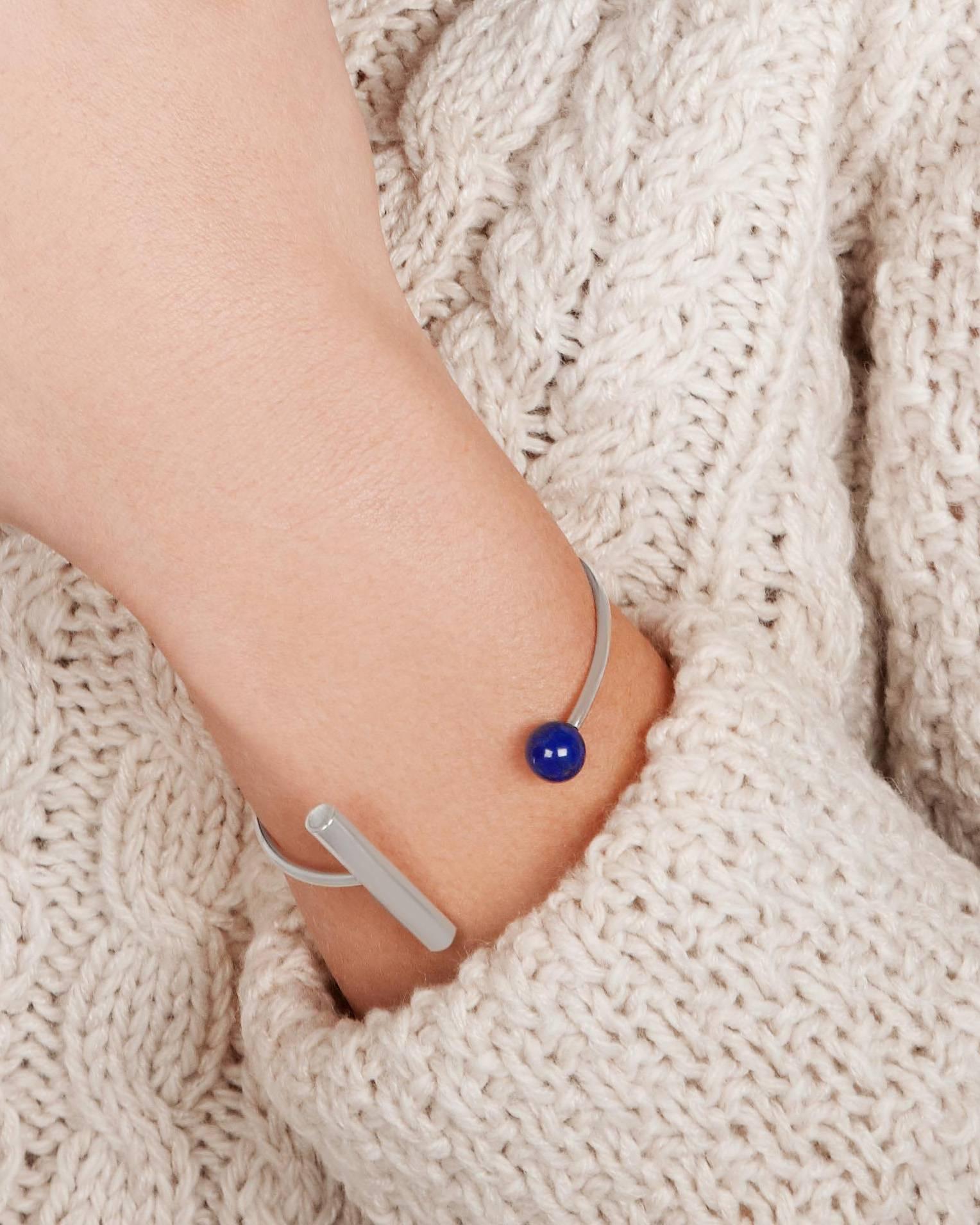 This striking cuff bracelet features a Modernist-inspired geometric design.  The bracelet is handcrafted in sterling silver with a natural lapis lazuli accent.  The bracelet is slightly flexible allowing for a customisable fit for the wearer.