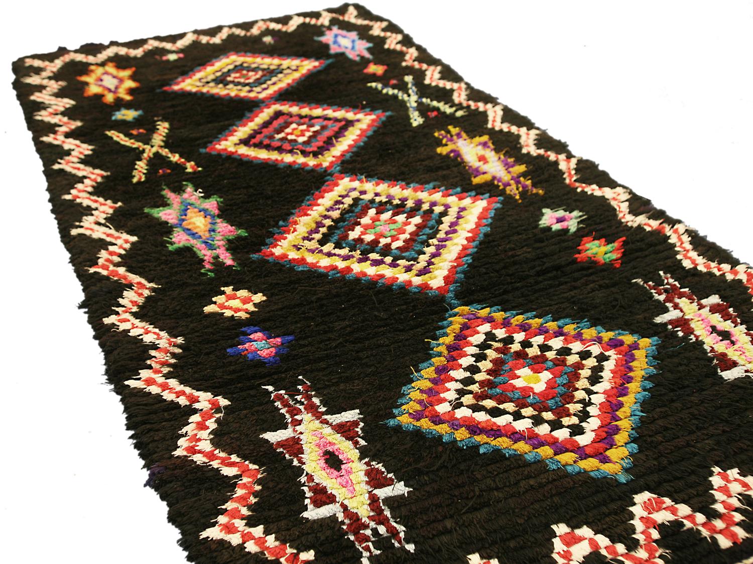 This is a semi-antique Moroccan Marrakesh rug woven circa 1950 and measures 176 x 91cm in size. This rug design incorporates four polychrome-colored center medallions flanked by star motifs set on a deep dark black background color. its main border