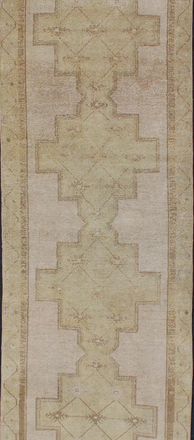 Leicht getönter türkischer Läufer mit Oushak-Muster, Teppich TU-ALK-3594, Herkunftsland/Typ: Türkei / Oushak, um 1940.

Dieser alte türkische Oushak-Läufer zeigt vier leicht gezeichnete, stilisierte Medaillons, die sich über das zentrale Feld