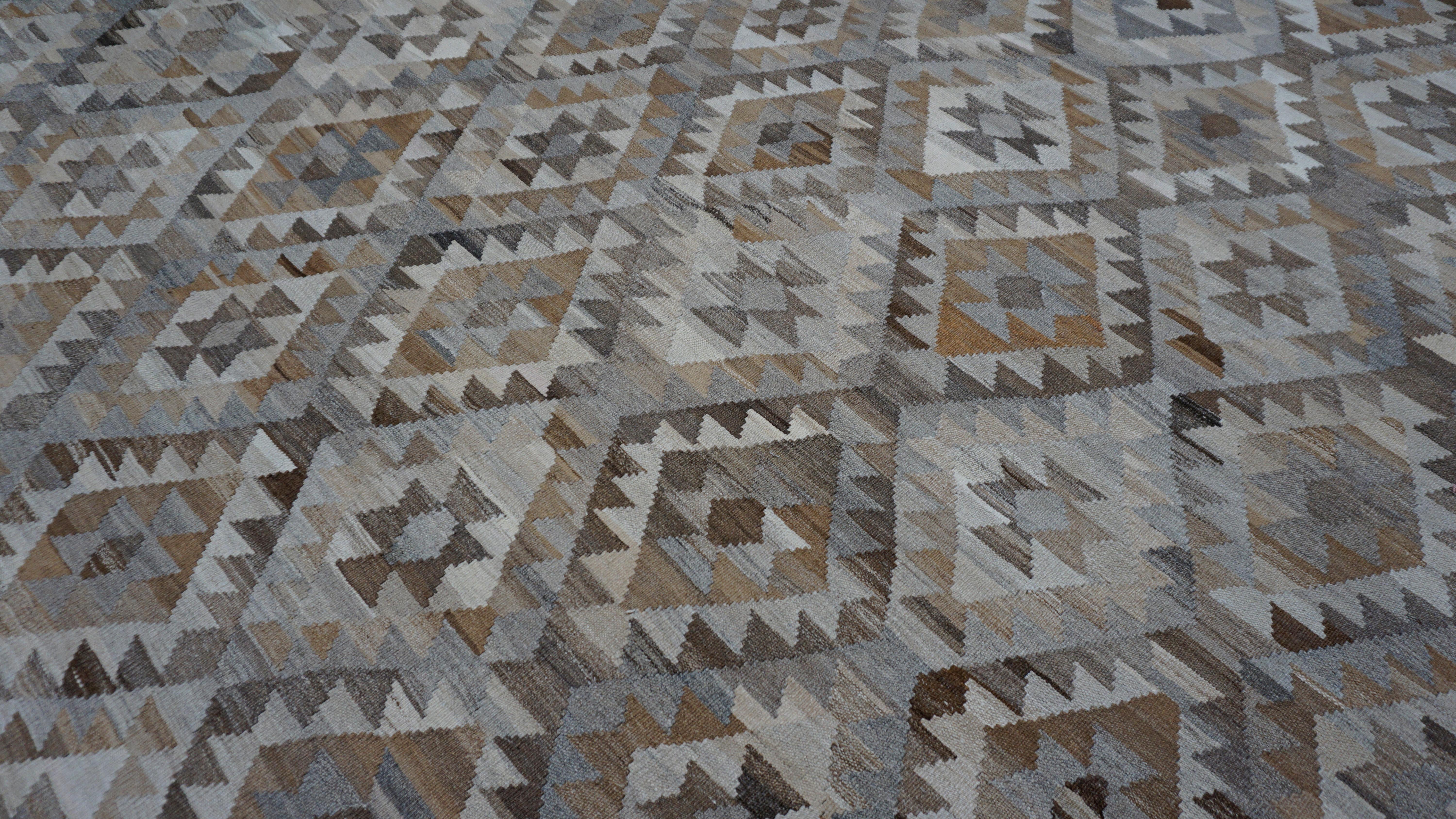 This striking handwoven wool kilim rug showcases a bold tribal geometric pattern inspired by traditional motifs. The repeating diamond lattice, filled with stepped medallions and arrow-like chevrons, creates a mesmerizing interplay of shape and