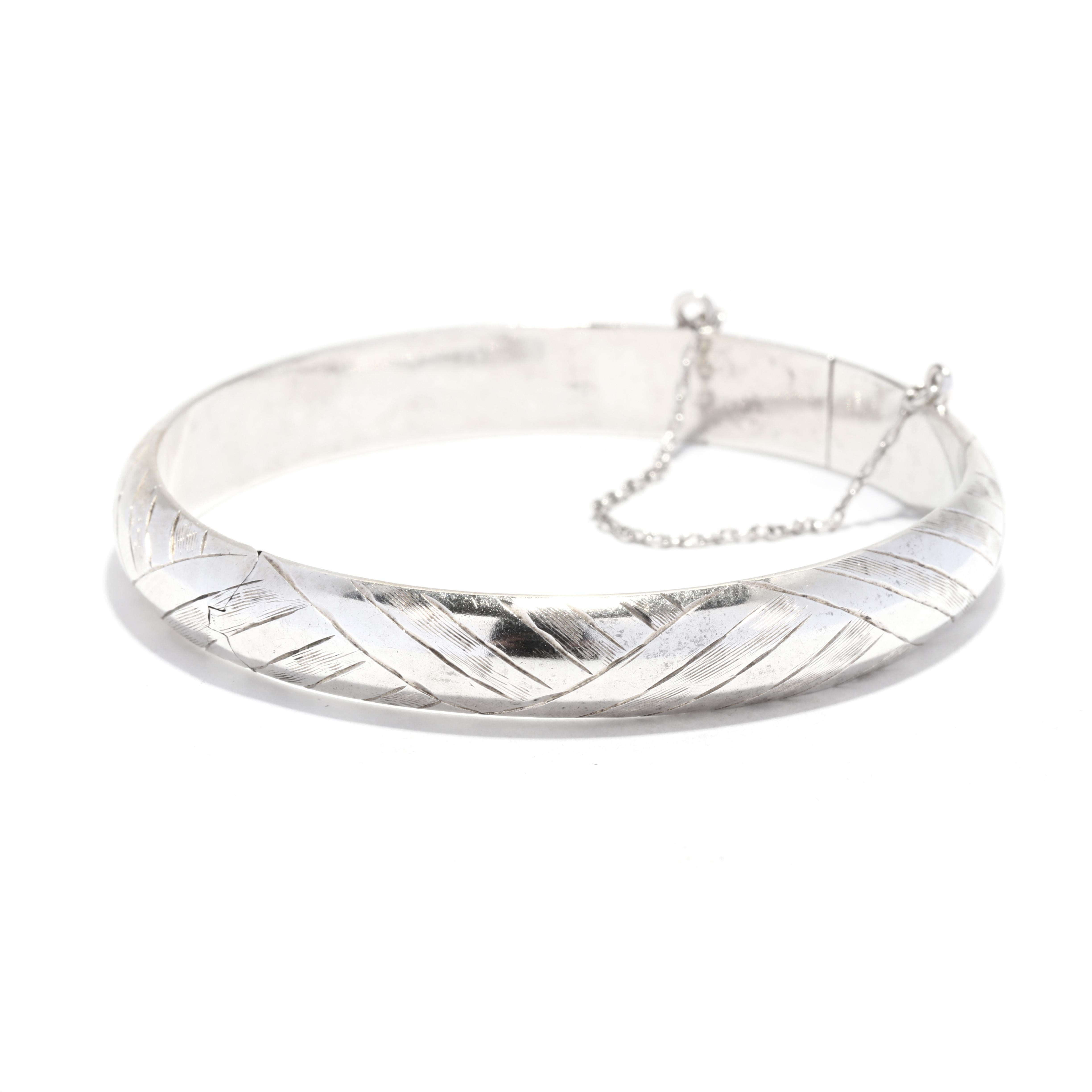 A vintage sterling silver geometric engraved hinged bangle bracelet. This stackable bangle features a domed design with a geometric engraved motif and with a hinged closure and safety chain.

Circumference: 7 in.

Width: 3/8 in.

Weight: 8 dwts. /