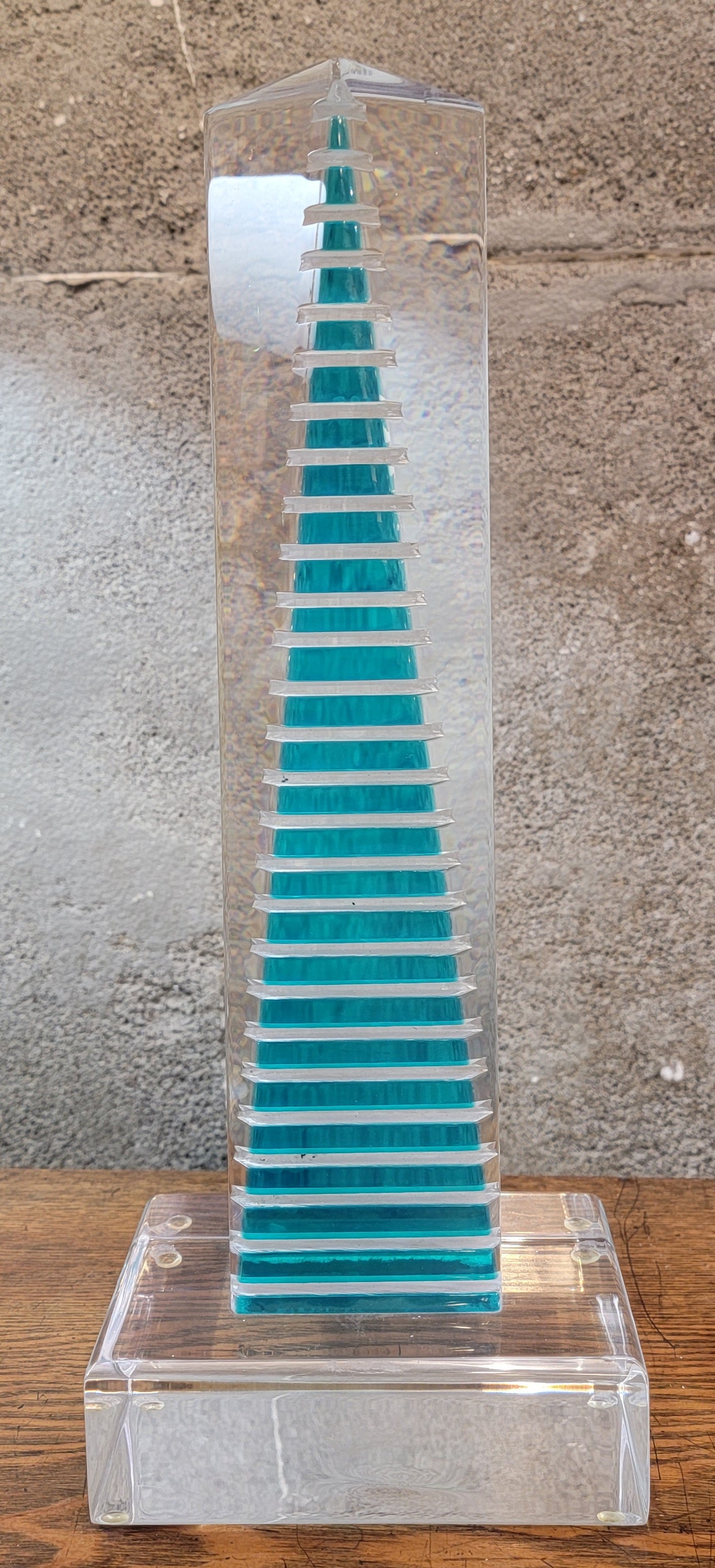 A Lucite or acrylic geometric sculpture. Diminishing aqua rectangles in clear Lucite monolith create an architectural skyscraper effect. Stands 15.75