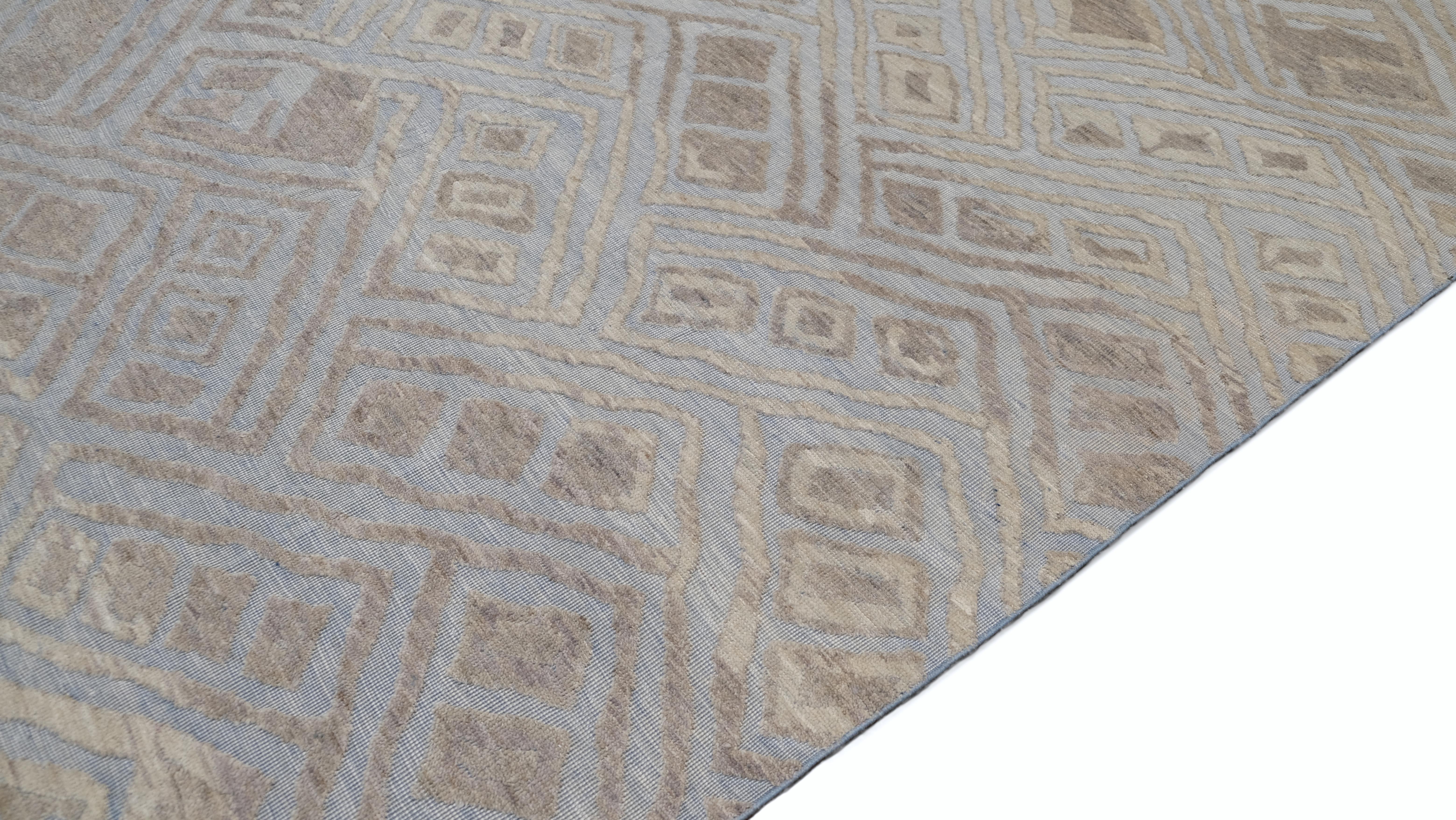 Dieser handgeknüpfte Wollteppich besticht durch ein geometrisches Rautenmotiv in einer eleganten Mischung aus weichen Beige- und gedämpften Blaugrautönen. Die filigrane Hoch-Tief-Struktur und das symmetrische Design erzeugen einen subtilen, aber