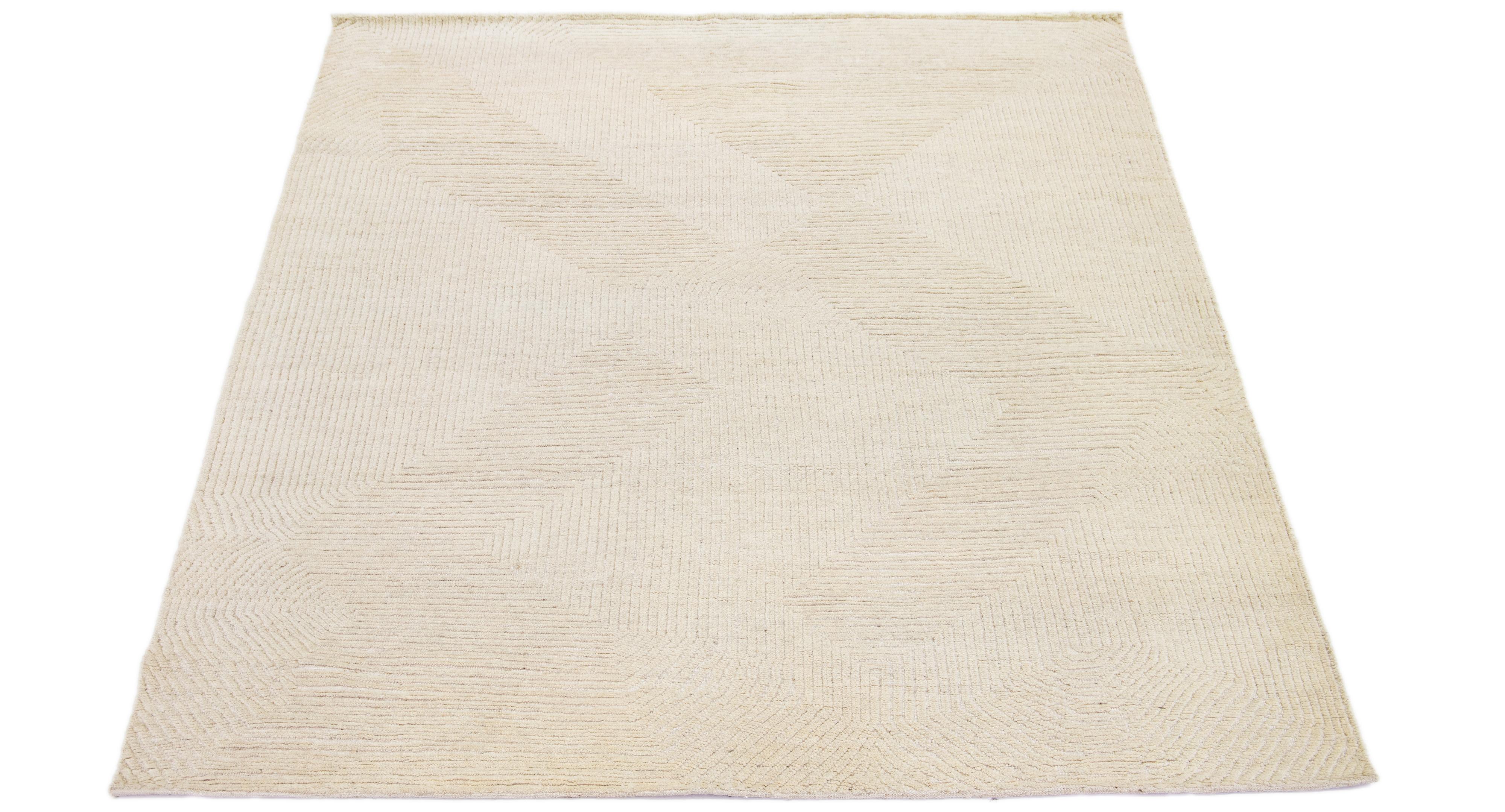 The wool rug, crafted with the hand-knotting technique, features a contemporary design inspired by Moroccan motifs. Its foundation boasts a natural beige shade that forms the backdrop of an appealing abstract geometric pattern.

This rug measures