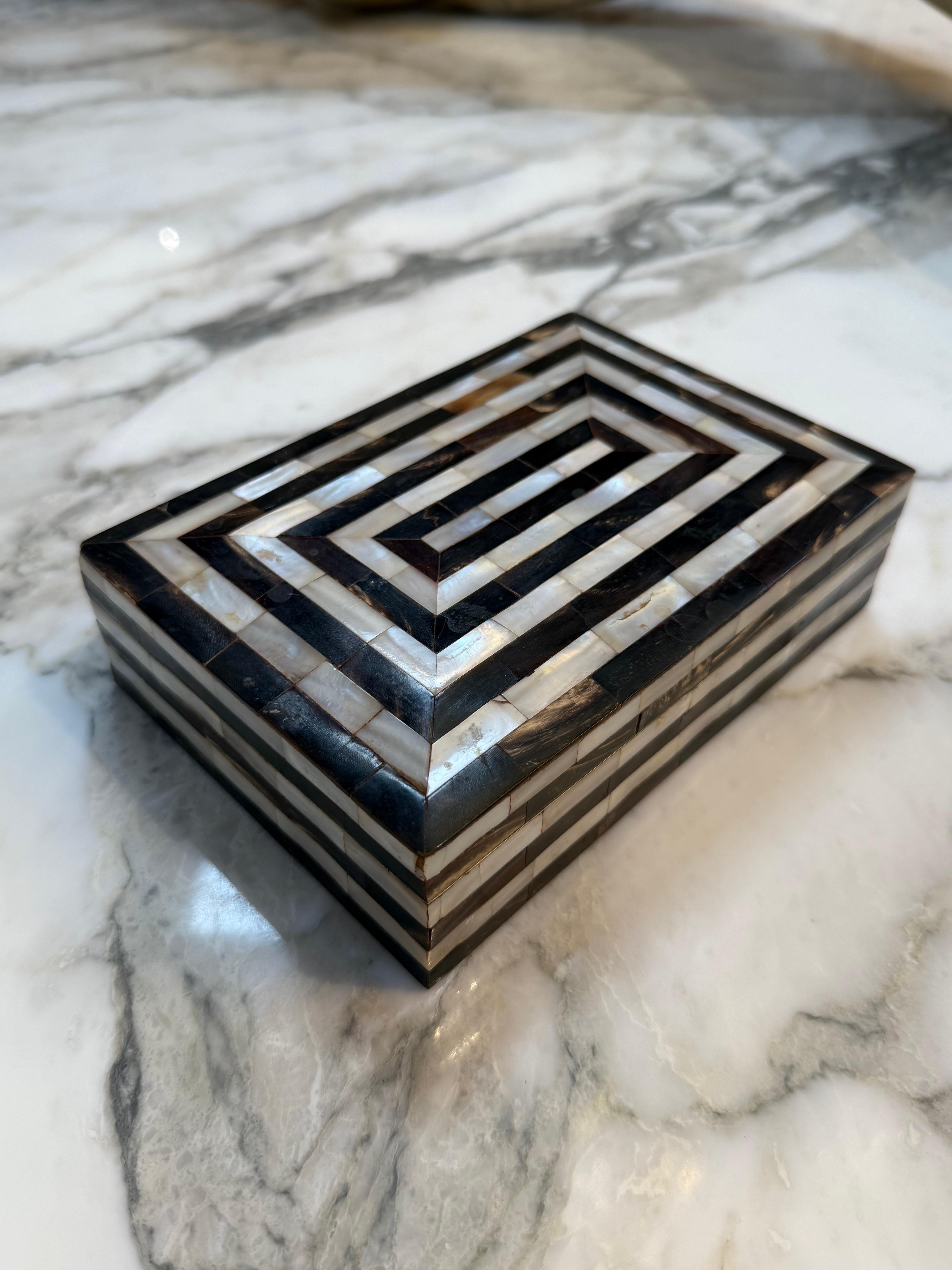 This elegant rectangular box showcases a striking geometric design created from alternating strips of dark horn and shimmering mother-of-pearl inlay. The pattern forms a mesmerizing concentric illusion that draws the eye toward the center, giving