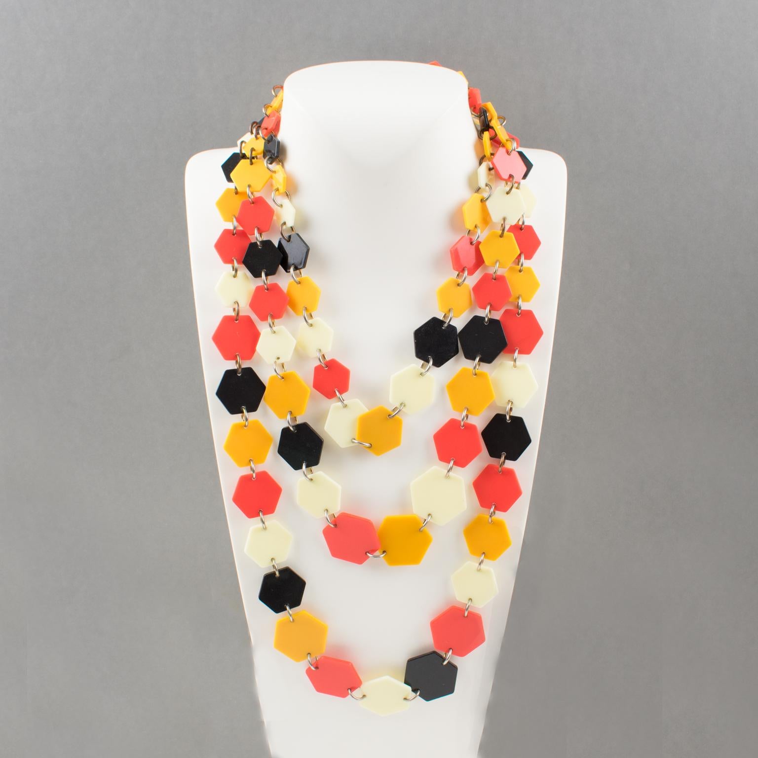 Questa sofisticata collana a più fili di design francese degli anni '70 presenta tre file graduali di elementi geometrici in lucite a forma di esagono piatto. Il pezzo vanta i colori tipici del periodo hippie: nero, arancione neon, giallo calendula