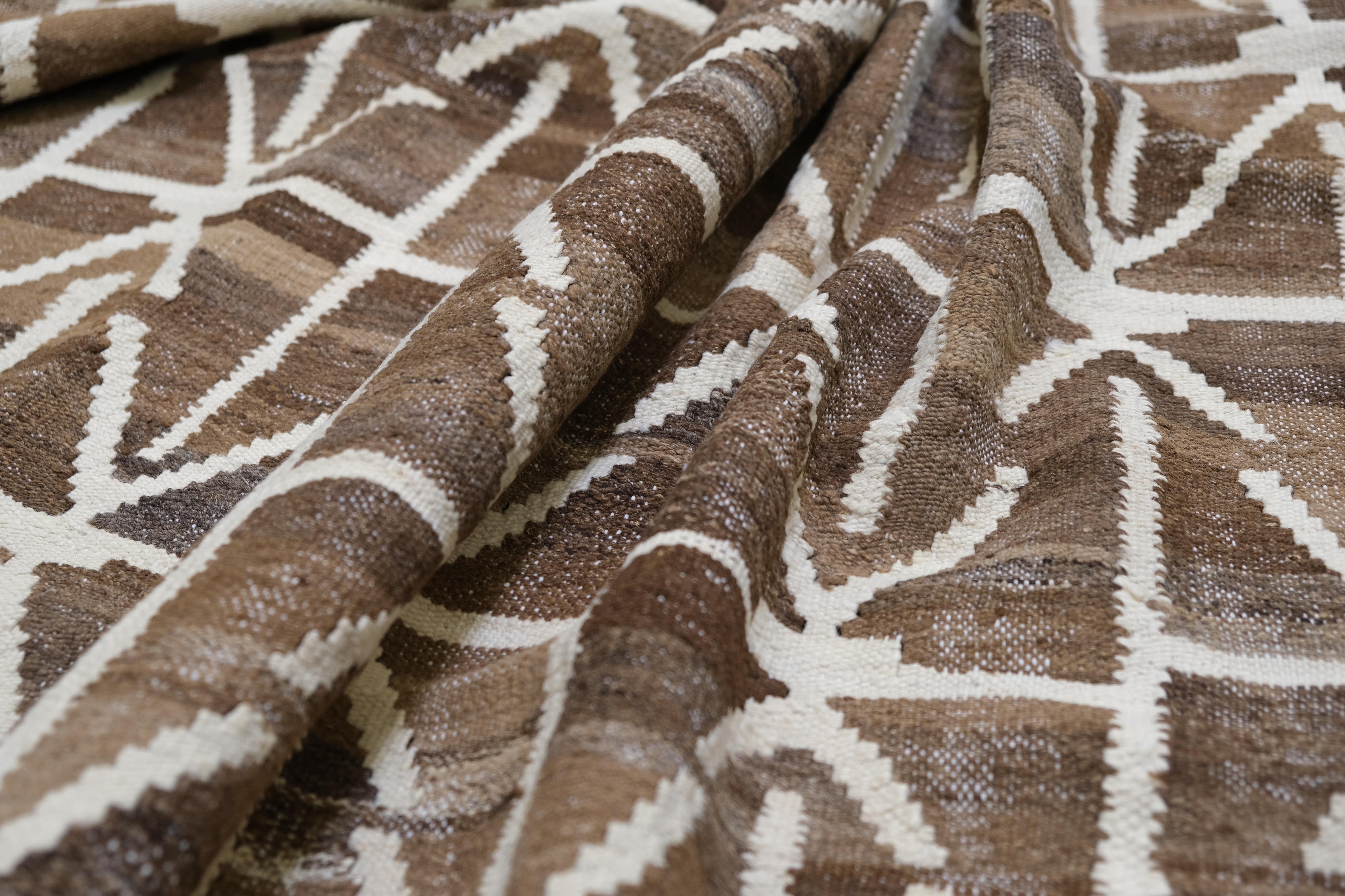 Ce magnifique tapis en laine tissé à la main au Pakistan est une véritable pièce d'apparat. Il présente un design géométrique saisissant composé de motifs imbriqués les uns dans les autres, dans de riches tons de terre. Alliant parfaitement