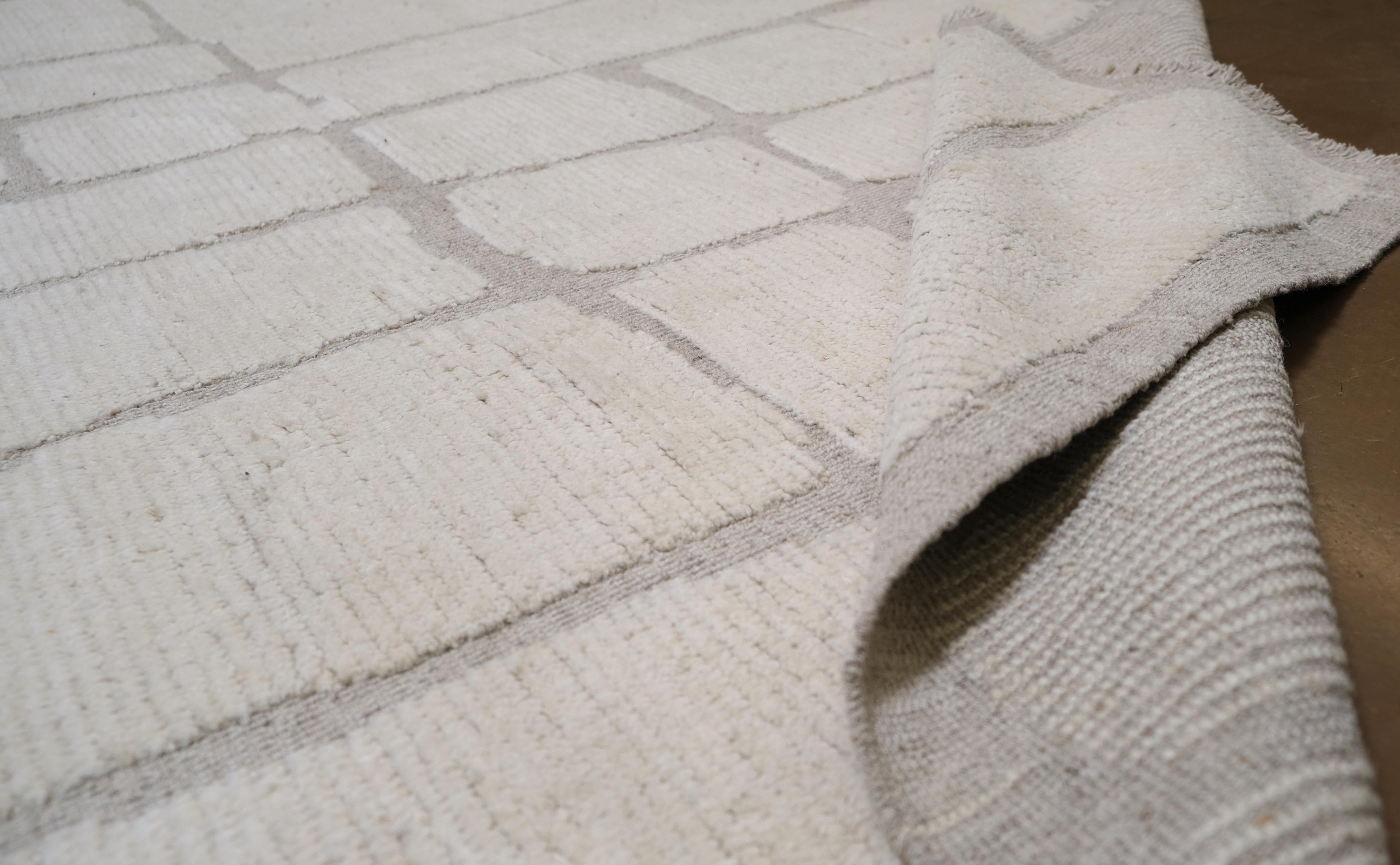 Elevate your home with the sophisticated charm of this hand-knotted wool rug from Pakistan, featuring a geometric pattern inspired by natural stone formations. The neutral tones and irregular grid-like design add an organic, yet modern aesthetic