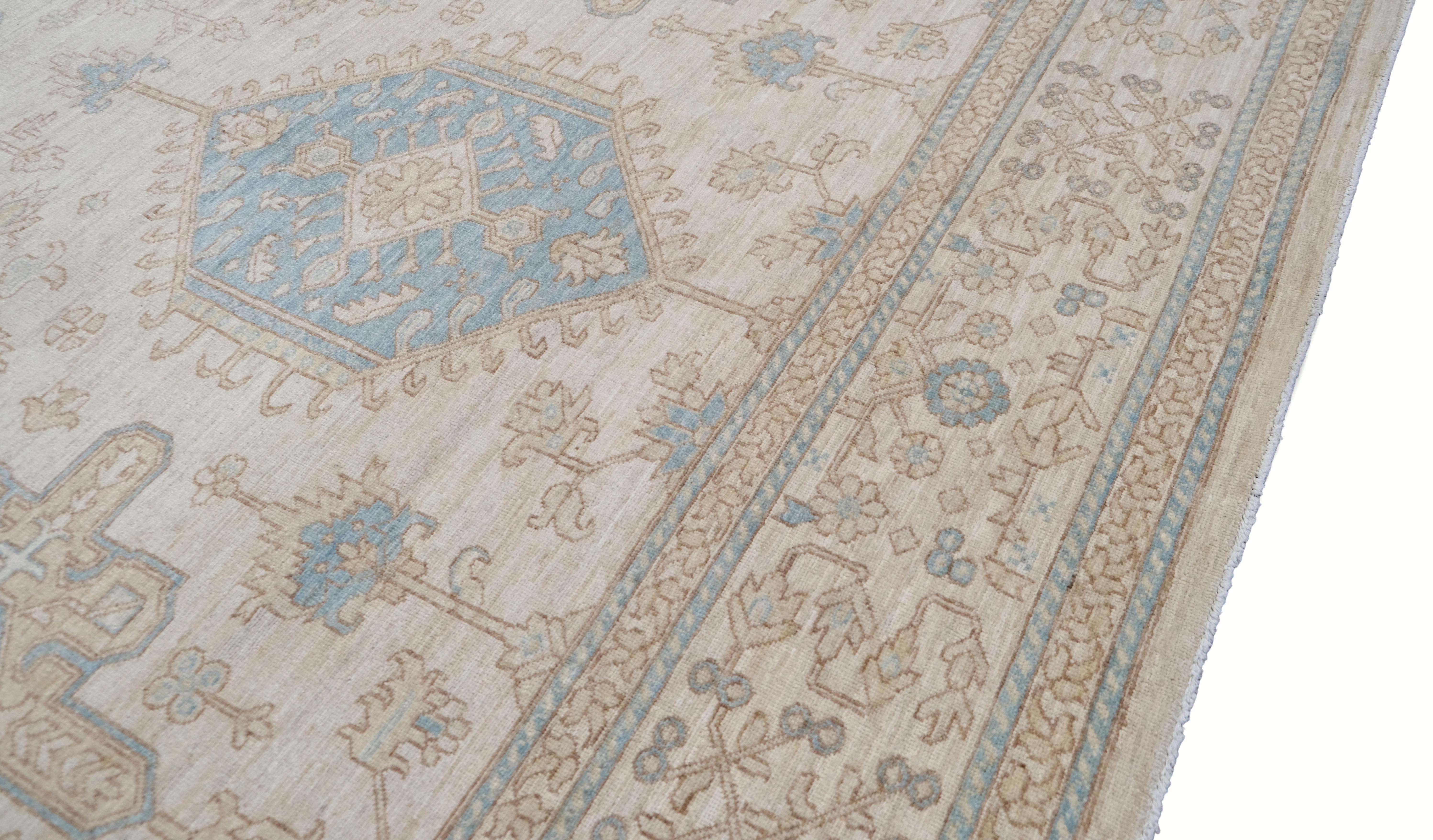 Esta alfombra de lana anudada a mano muestra un tradicional diseño floral geométrico oushak en suaves tonos beige y azul apagado. Con intrincados diseños de medallones y delicados motivos de enredaderas, esta alfombra encarna la elegancia de los