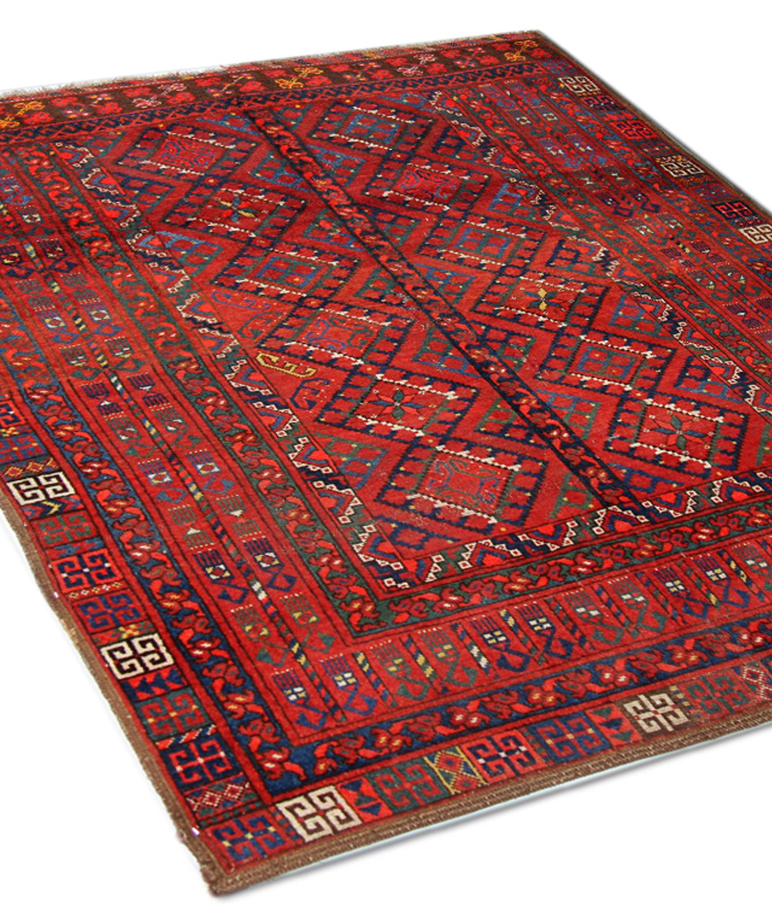 This wool rug is an impressive example of l hand-knotted carpets hand-woven in the early 20th century. It features a bright red background that contrasts beautifully with the geometric details woven in green and blue. The design features a geometric
