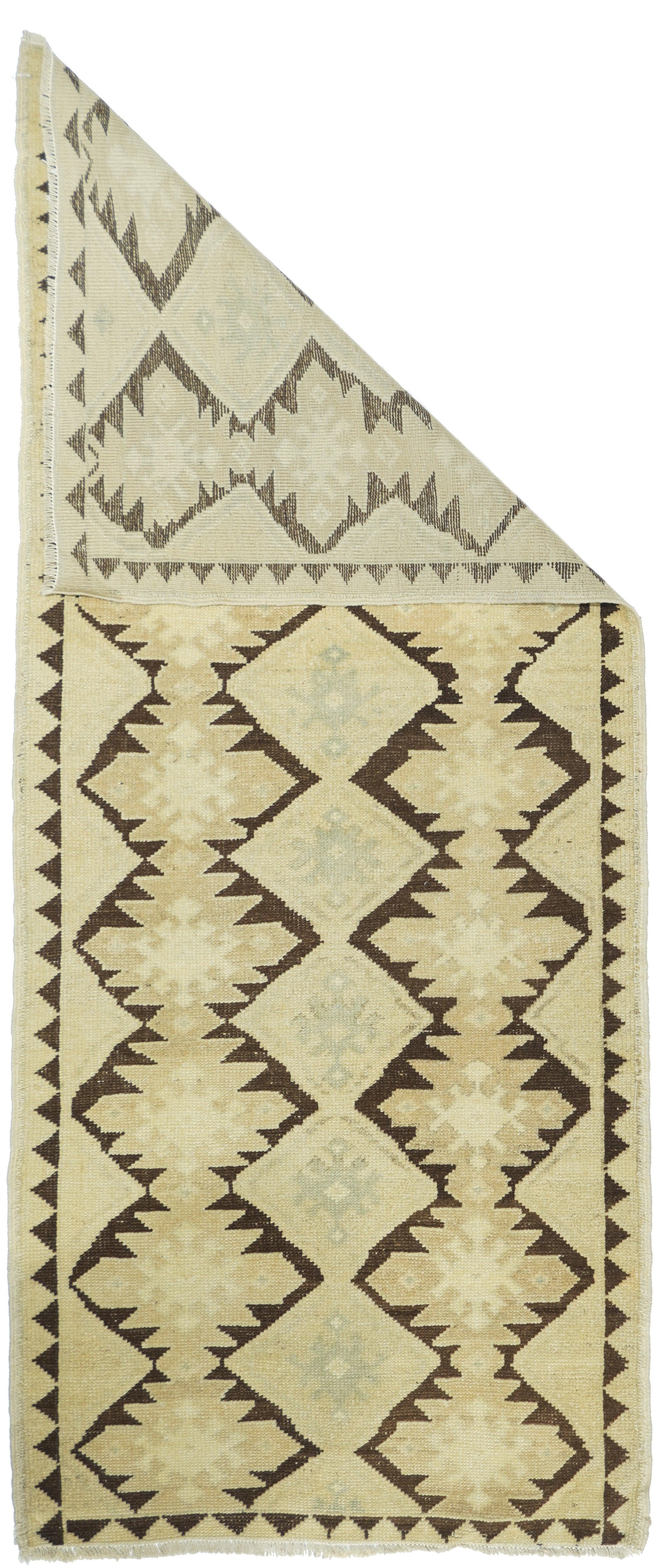 Tappeto geometrico  2'7'' x 7'1''. Figura contro terra. Il campo rosso-marrone mostra due colonne di ashik che racchiudono diamanti uncinati color paglierino chiaro, con medaglione di pali color paglierino/beige al centro e mezzi pali en suite ai