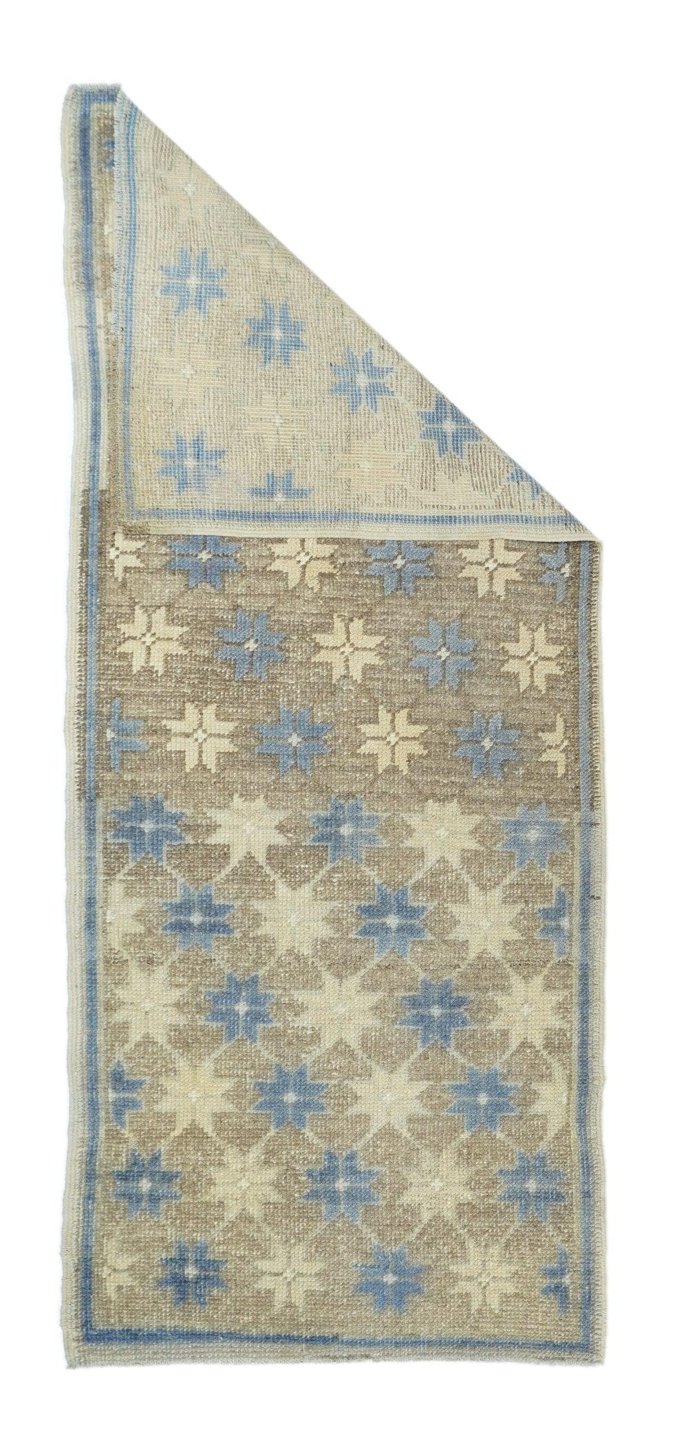 Geometrischer Teppich 2'8'' x 6'9''. Das bräunliche Korallenfeld zeigt abwechselnd Diagonalen von achtspitzigen Sternen in Hellblau und Stroh innerhalb eines Rautengitters mit Farbwechsel. Hellblauer schmaler Linienrand. Basis Wolle, mittlere