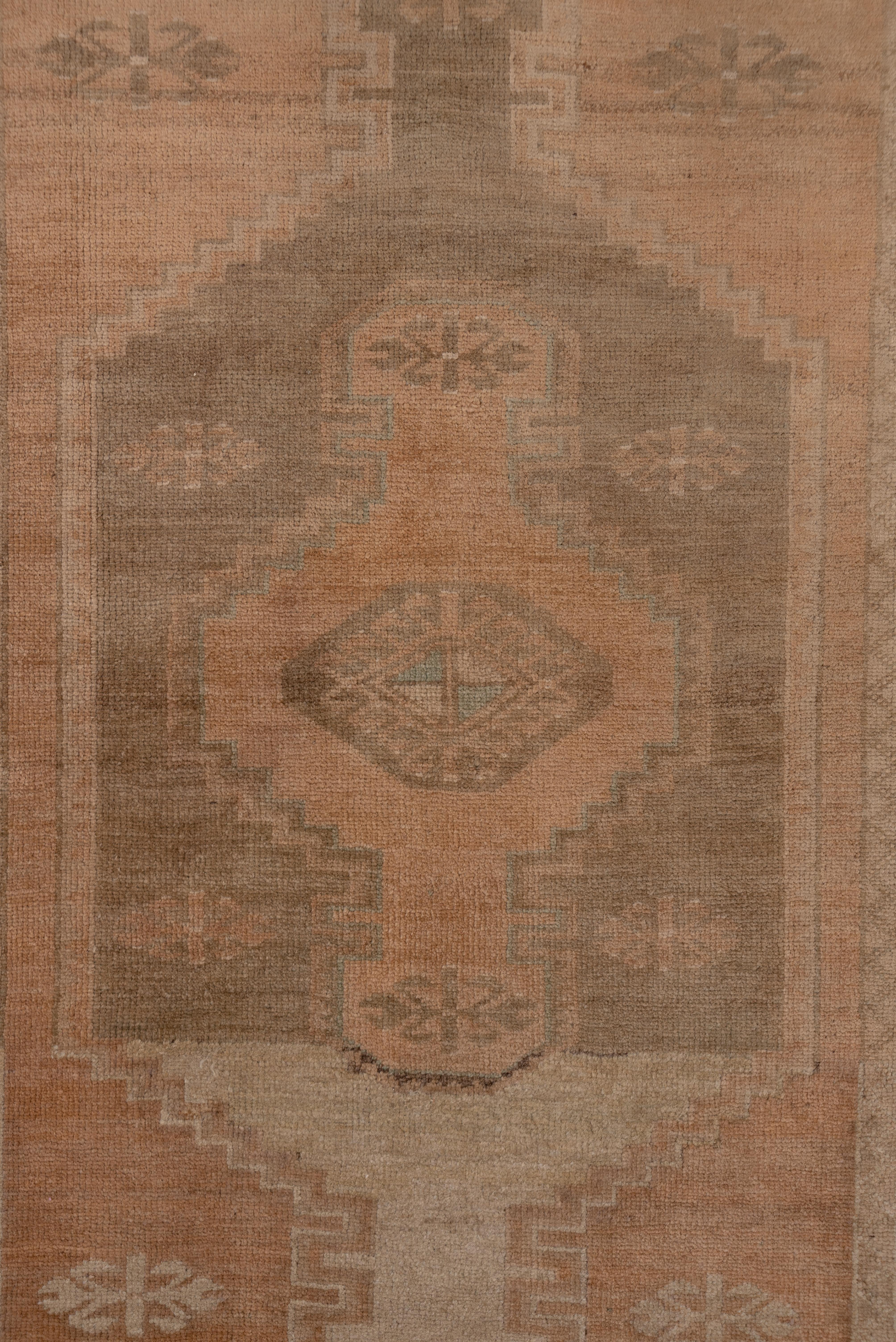 This eastern Turkish narrow runner features an abrashed soft salmon ground with three complete end stepped cartouche medallions in sand, pale coral, and ecru beige. The abrash extends to the zig-zag narrow border.