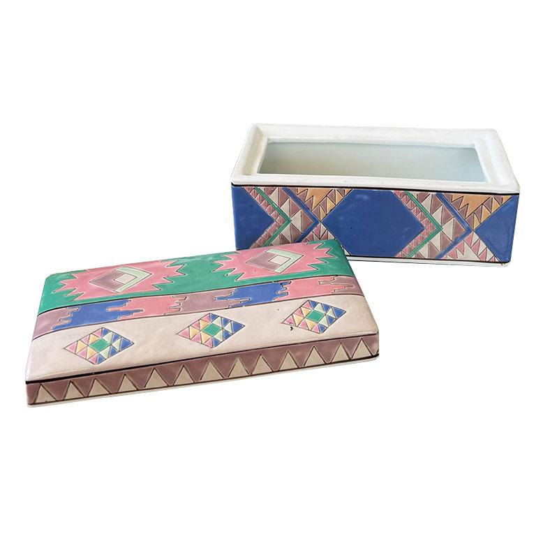 A long rectangular ceramic box in a Southwest or Geometric motif. We've never seen a box like this before. The sides are painted in a deep blue with geometric patterns in bright green, peach, pink, and orange. The lid fits snugly onto the bottom and