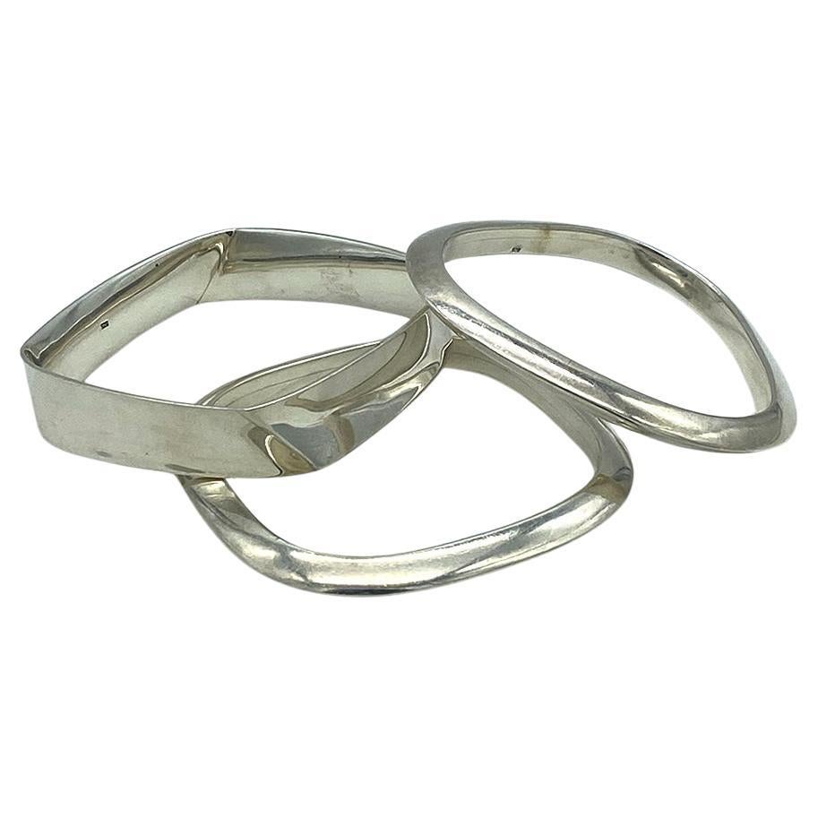 This is a set of geometric sterling silver bangles. The 110g total weight of three bangles comes with two square and one triangle shaped with round corners. Two of the bangles have a solid triangular cross-section. One of the square bangles has a