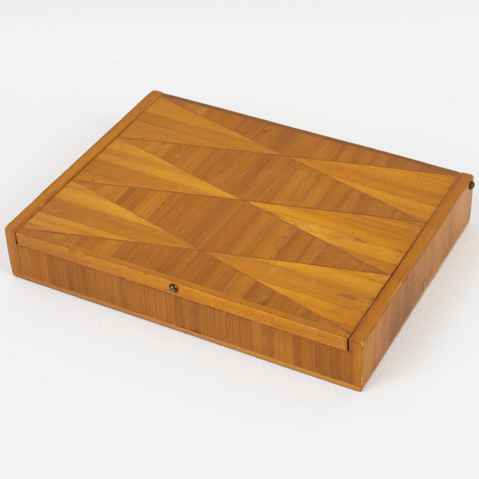 Esta elegante caja con tapa decorativa de marquetería de paja tiene su diseño atribuido al diseñador francés Jean Michel Frank (1895 - 1941). La forma rectangular alargada tiene un refinado diseño geométrico, y el interior está forrado de corcho. No
