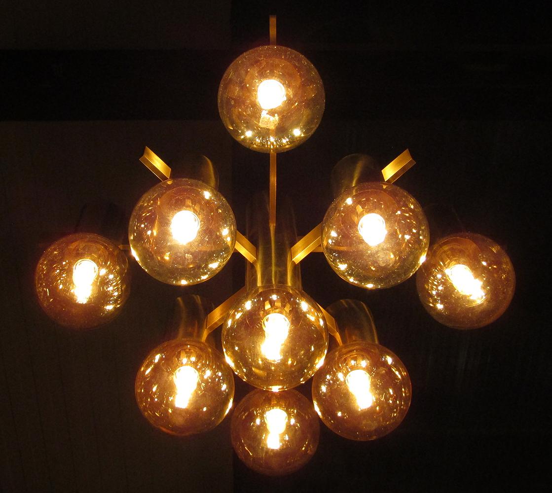 A geometric 1970s chandelier with opalescent art glass shades by Swedish designer Hans-Agne Jakobsson.

It has nine individual lights on three tiers supported by eight brushed brass arms. It emits a soft, warm light. It will make a striking