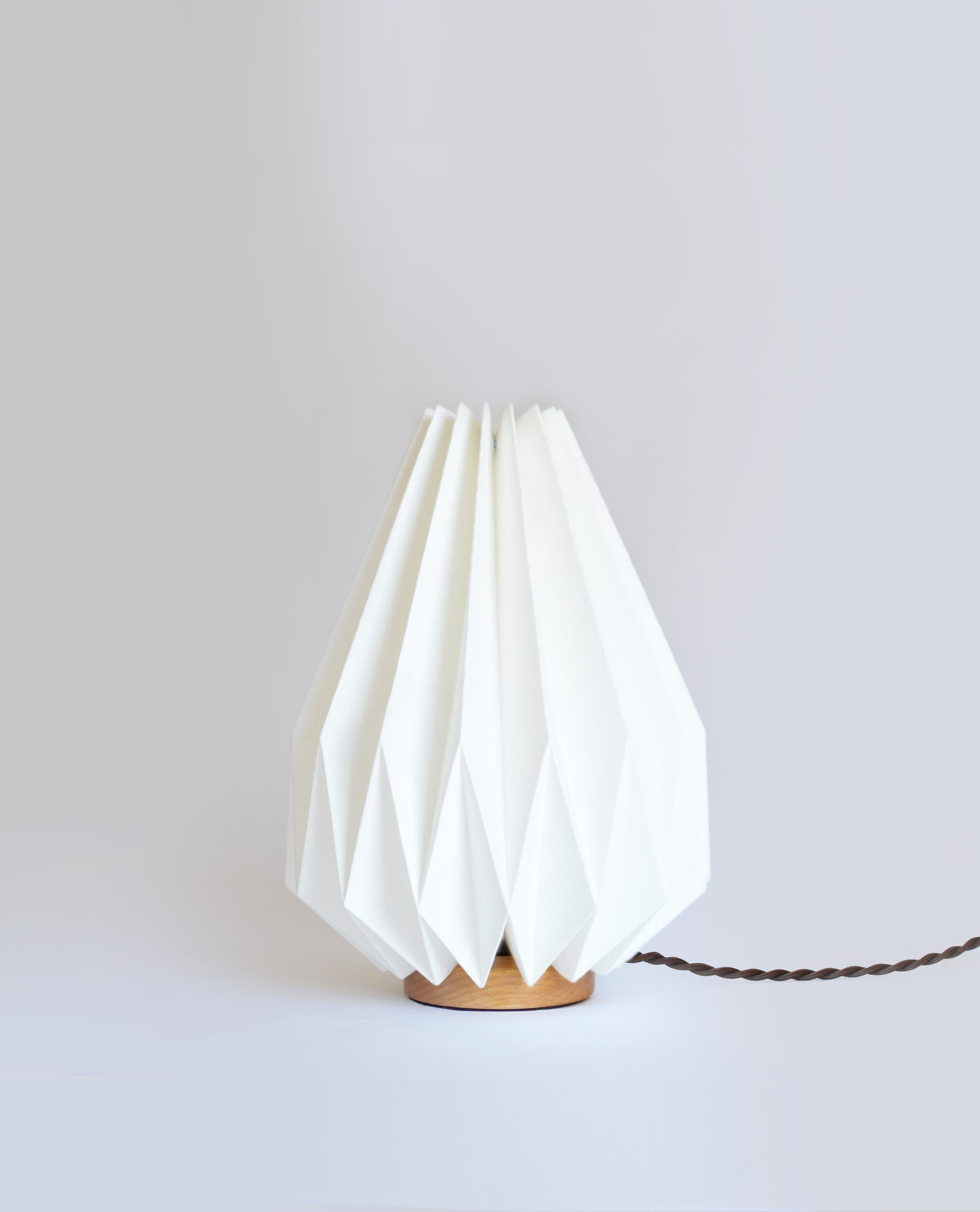 Made of a linen shade with a simple handcrafted wooden base, this table lamp will bring to your interior an interesting and functional work of art. The origami-inspired lampshade provides a bright, yet soft ambient light and shows the beautiful