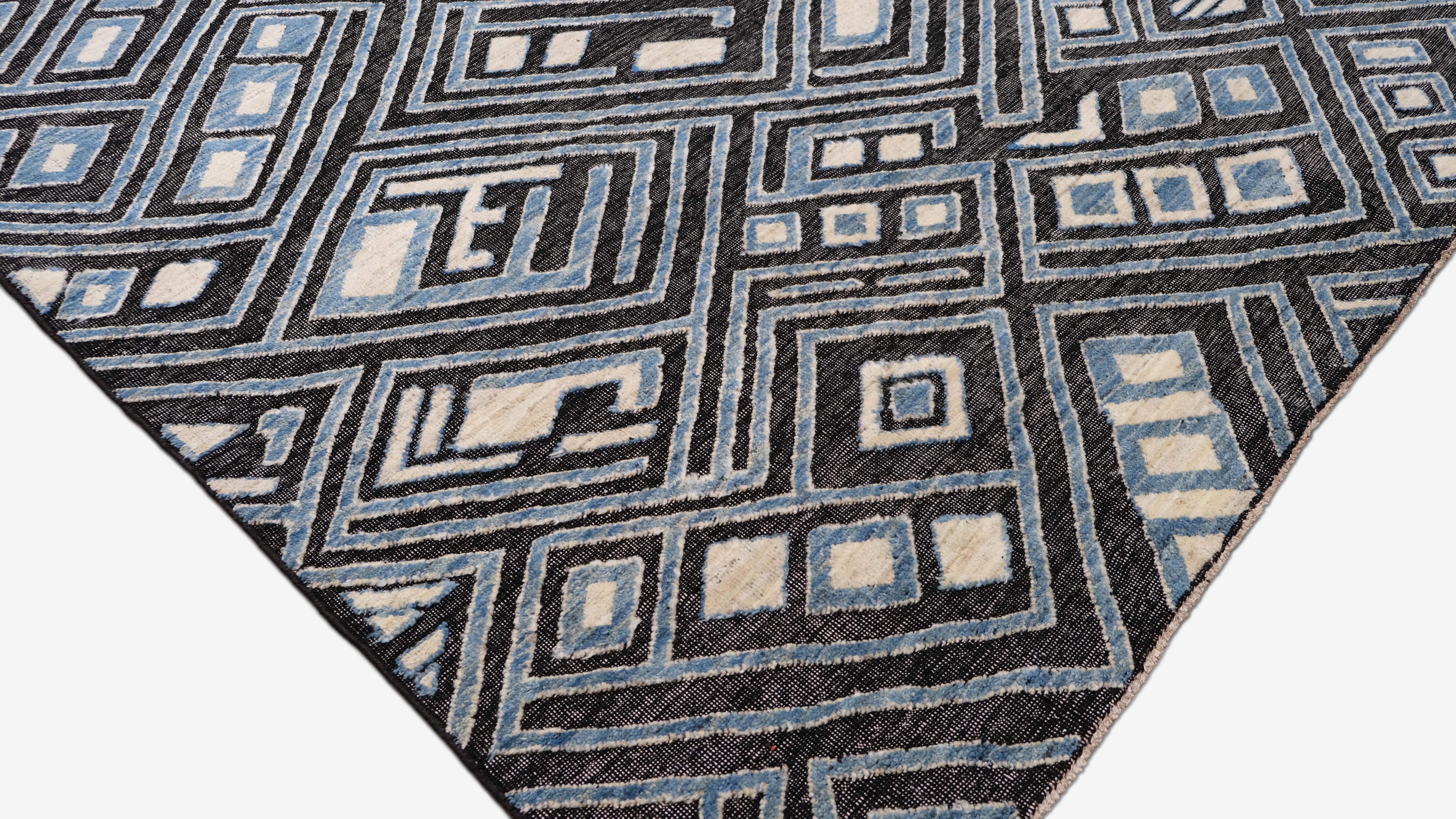 Questo tappeto in lana annodato a mano presenta un audace motivo geometrico tribale, caratterizzato da un intricato gioco di motivi a rombi angolari nelle tonalità del blu cielo intenso, del carbone e dell'avorio. Il design dinamico a strati e la