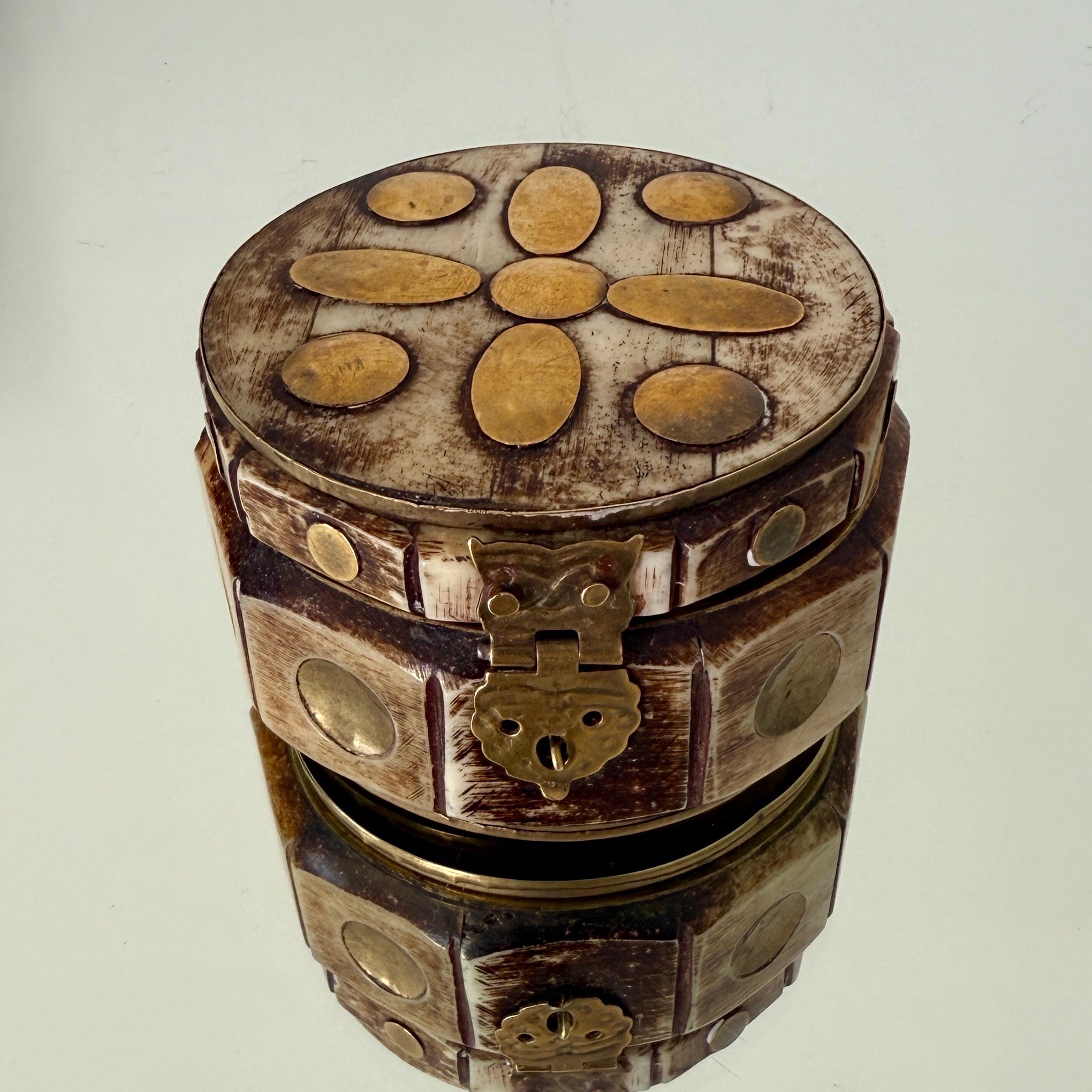Handmade brass metal and bone trinket box with inlays.  The round box has a geometric design with ten sides that feature brass circle inlays within the carved bone frame.  The box has a raised base, a lidded top, and brass interior.  Great as