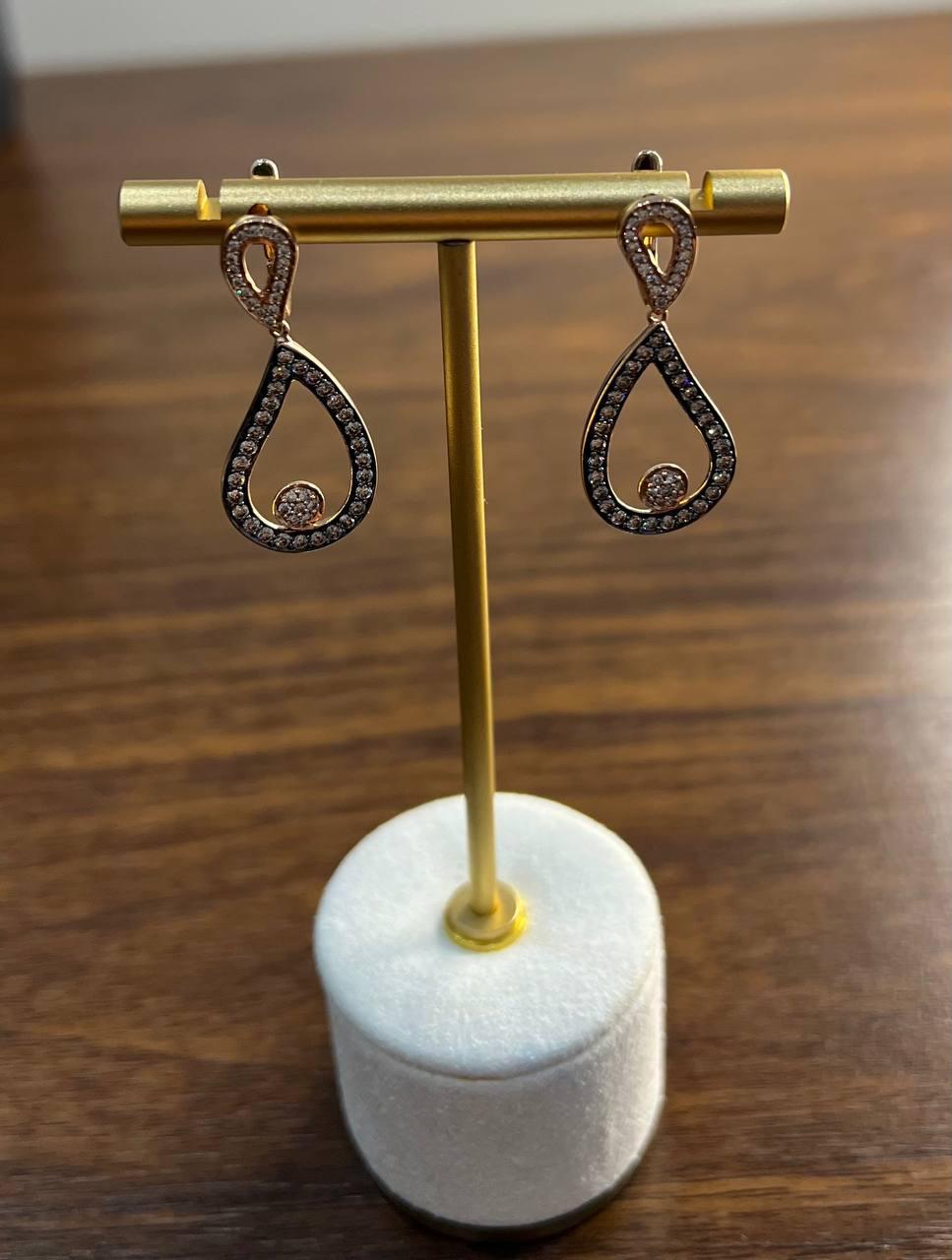 The earrings feature a graceful teardrop design, adorned with shimmering white and champagne diamonds that catch the light beautifully. The intricate loop at the top adds a touch of sophistication, while the gold setting enhances the brilliance of