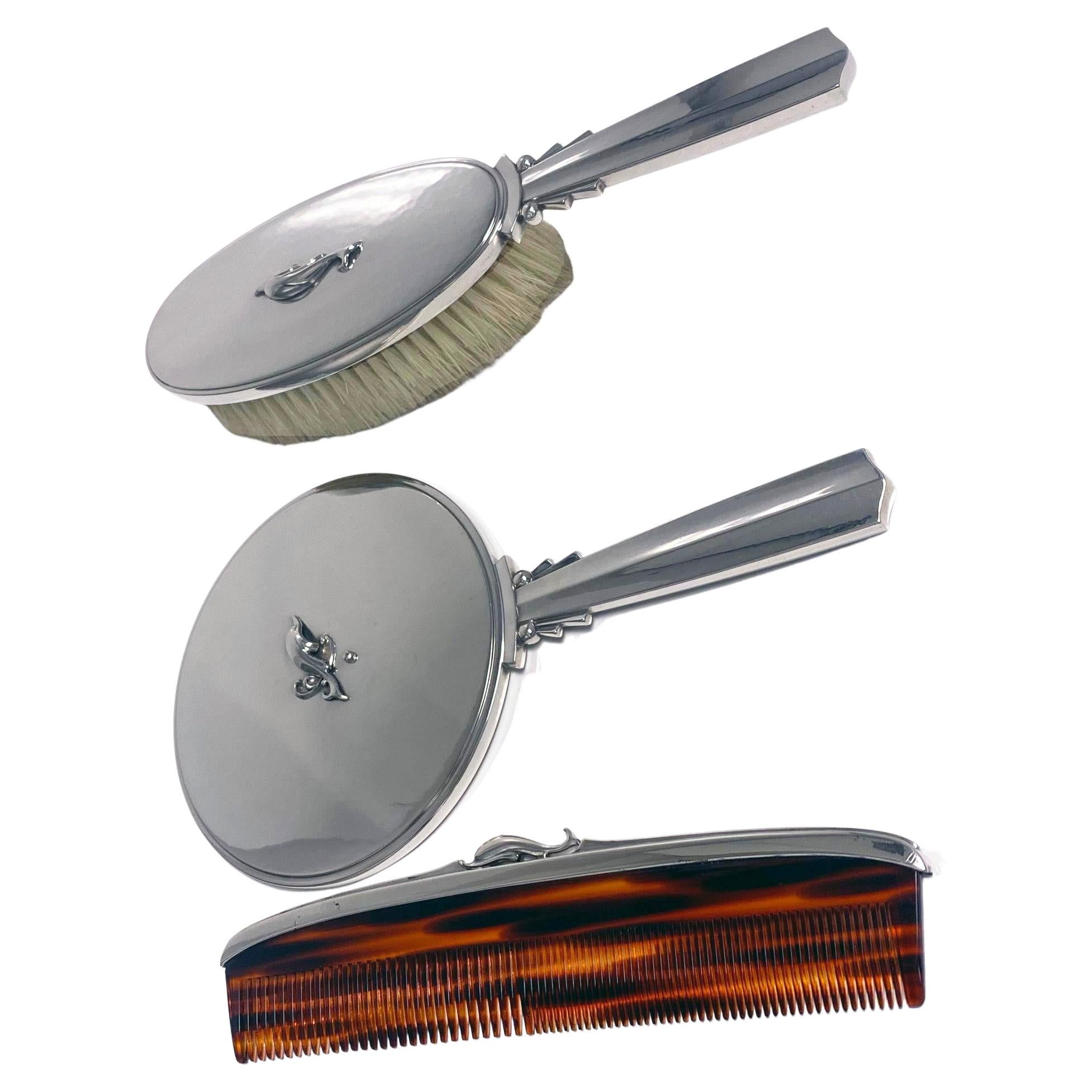 Georg Jensen Art Deco sterling silver vanity set Dolphin pattern. The set comprising Hand Mirror, Brush and Comb, designed by Harald Nielsen. Lengths of Mirror and Brush 8.75 inches; Comb 7.75 inches. Light hammered design with dolphin accents. Very