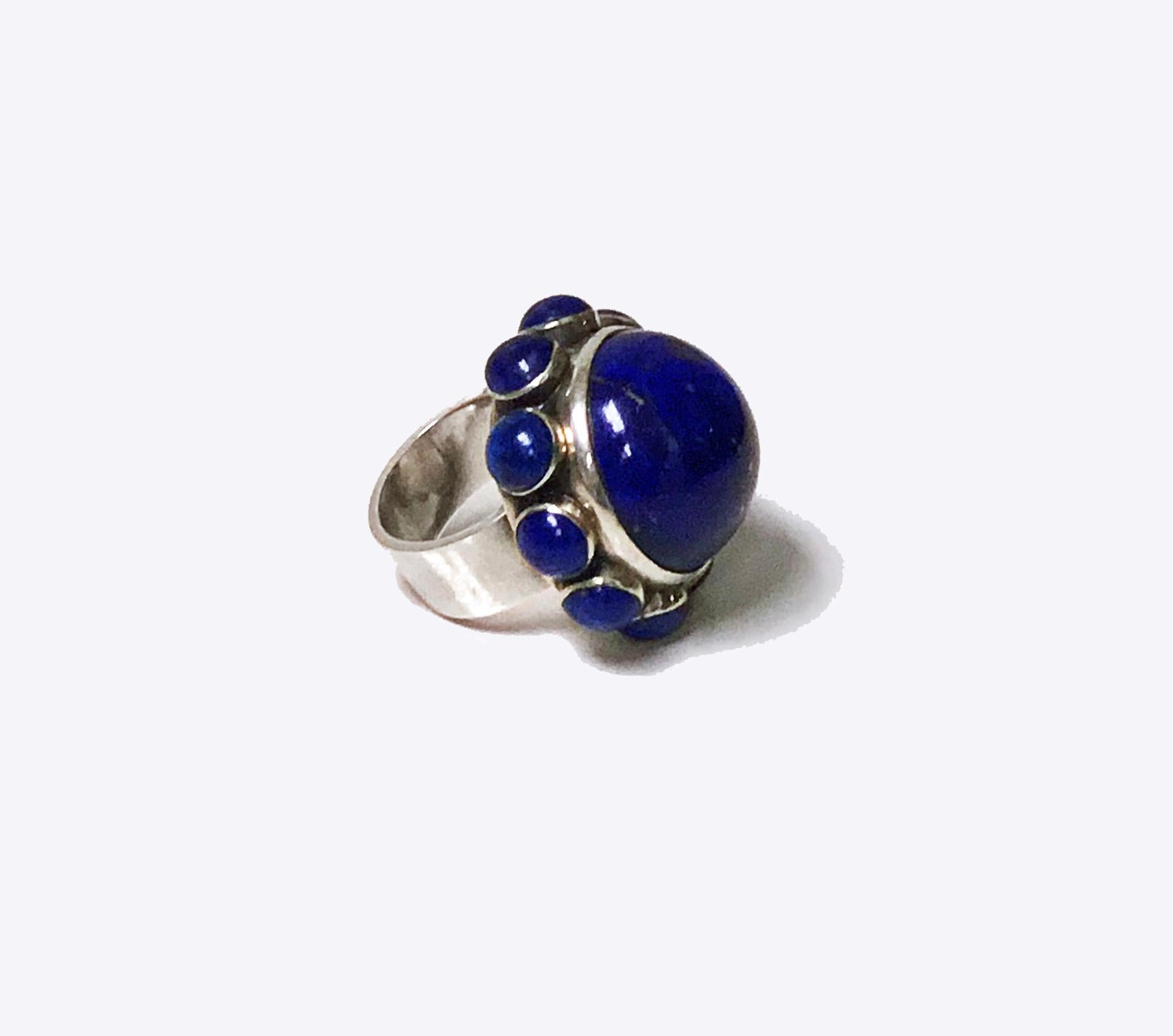 Georg Jensen Astrid Fog Lapis Ring C.1971 No 166. The centre with large cabochon fine Lapis Lazuli surrounded by ten smaller cabochon lapis lazuli. Top Diameter: approximately 1.25 inches. Height of mount: Approximately 7/8 inches. Ring Size: 7.