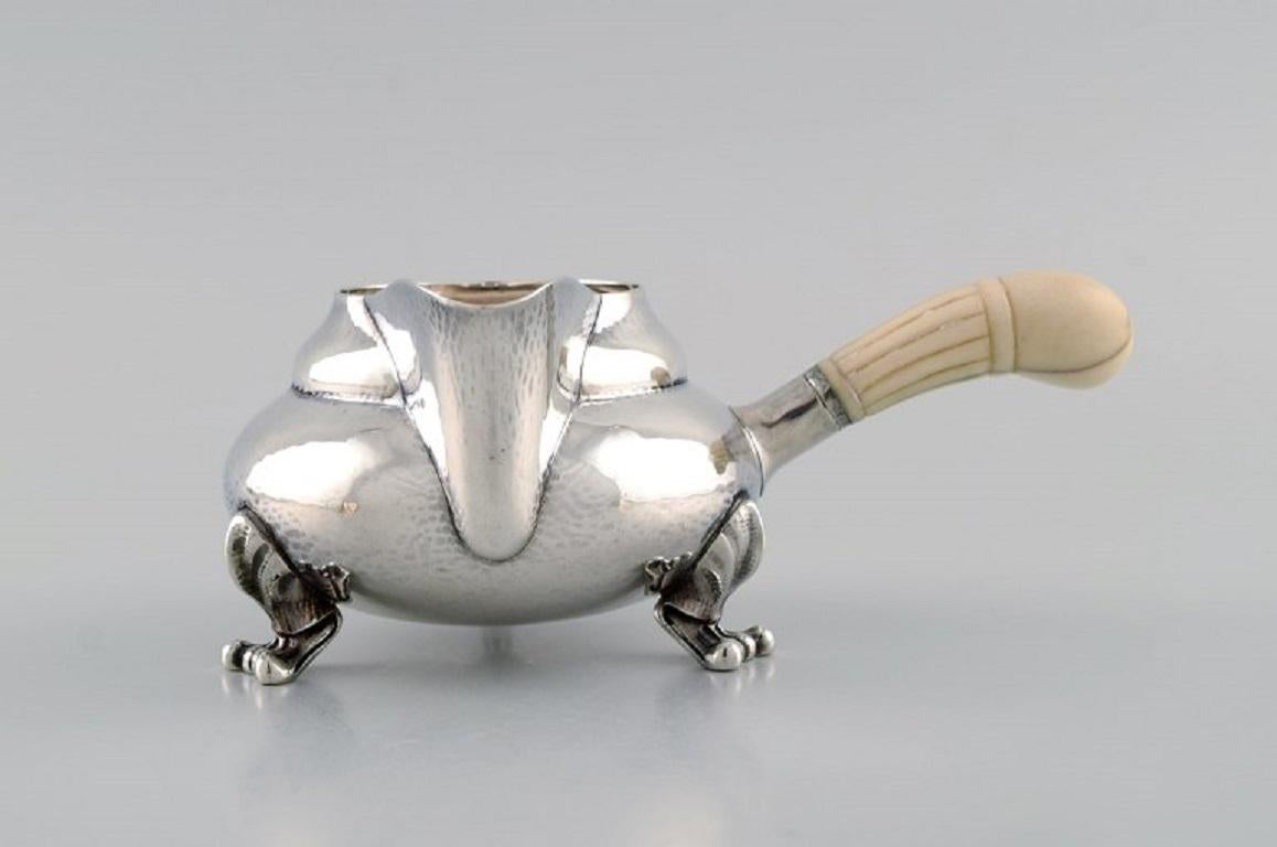 Crémier Blossom de Georg Jensen en argent sterling martelé avec une poignée ivoire. Modèle 2C. Daté de 1915-1930.
Mesures : 15,5 x 6,5 cm (y compris la poignée).
En parfait état. Usure minimale liée à l'âge.
Estampillé.
Notre orfèvre Georg