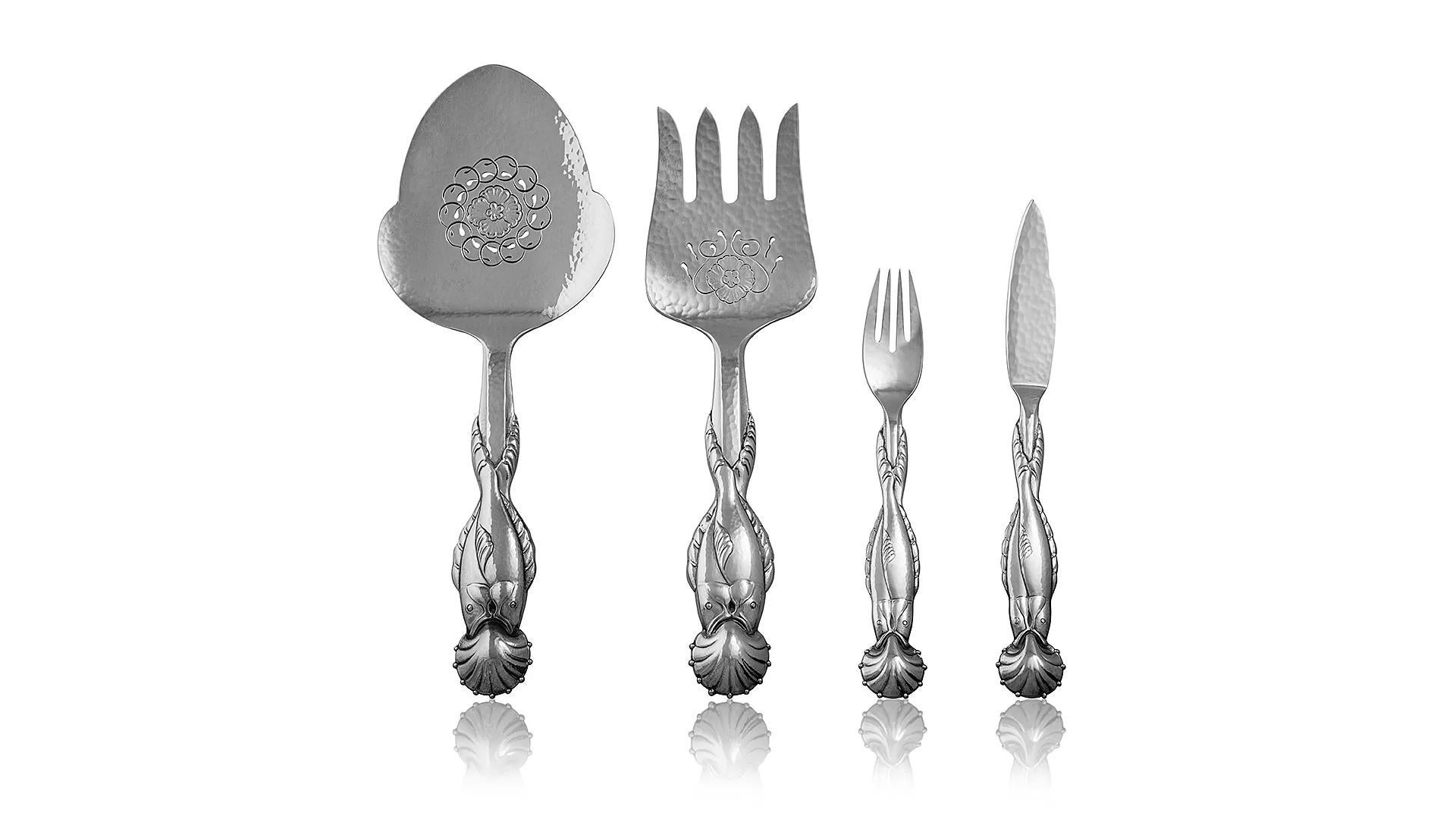 An unused sterling silver fish service for twelve with a matching serving set in the Georg Jensen silverware pattern #55, designed by Georg Jensen in year 1914. The handles feature two entwined fish, with a shell finial. The serving ends are