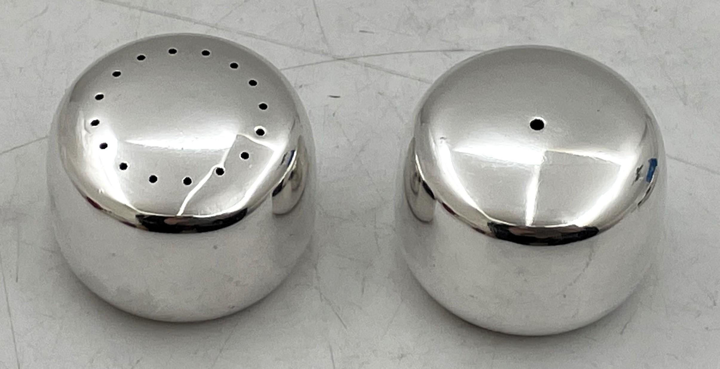 Pareja de saleros y pimenteros Georg Jensen de plata de ley, diseñados por Henning Koppel con el número de modelo 1135, y de estilo Moderno de Mediados de Siglo, con un elegante diseño geométrico. Miden 1 1/3'' de diámetro por 1'' de altura, pesan