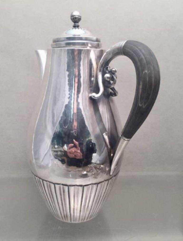 Magnificent sterling silver tea pot by the famous Danish maker, Georg Jensen in the highly desirable Cosmos pattern designed by Johan Rohde with wooden handle. Measuring approximately 10 inches tall and 7 1/2 inches form handle to spout. Weighing 21