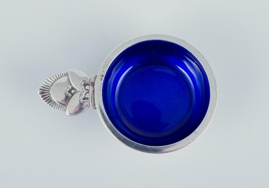 Georg Jensen Cactus. 
Salt cellar in sterling silver with accompanying salt spoon. 
Interior with royal blue enamel.
Model number 30.
Hallmarked after 1944.
In perfect condition.
Spoon: Length 5.5 cm.
Salt cellar: Length 6.5 cm. x 1.5 cm.